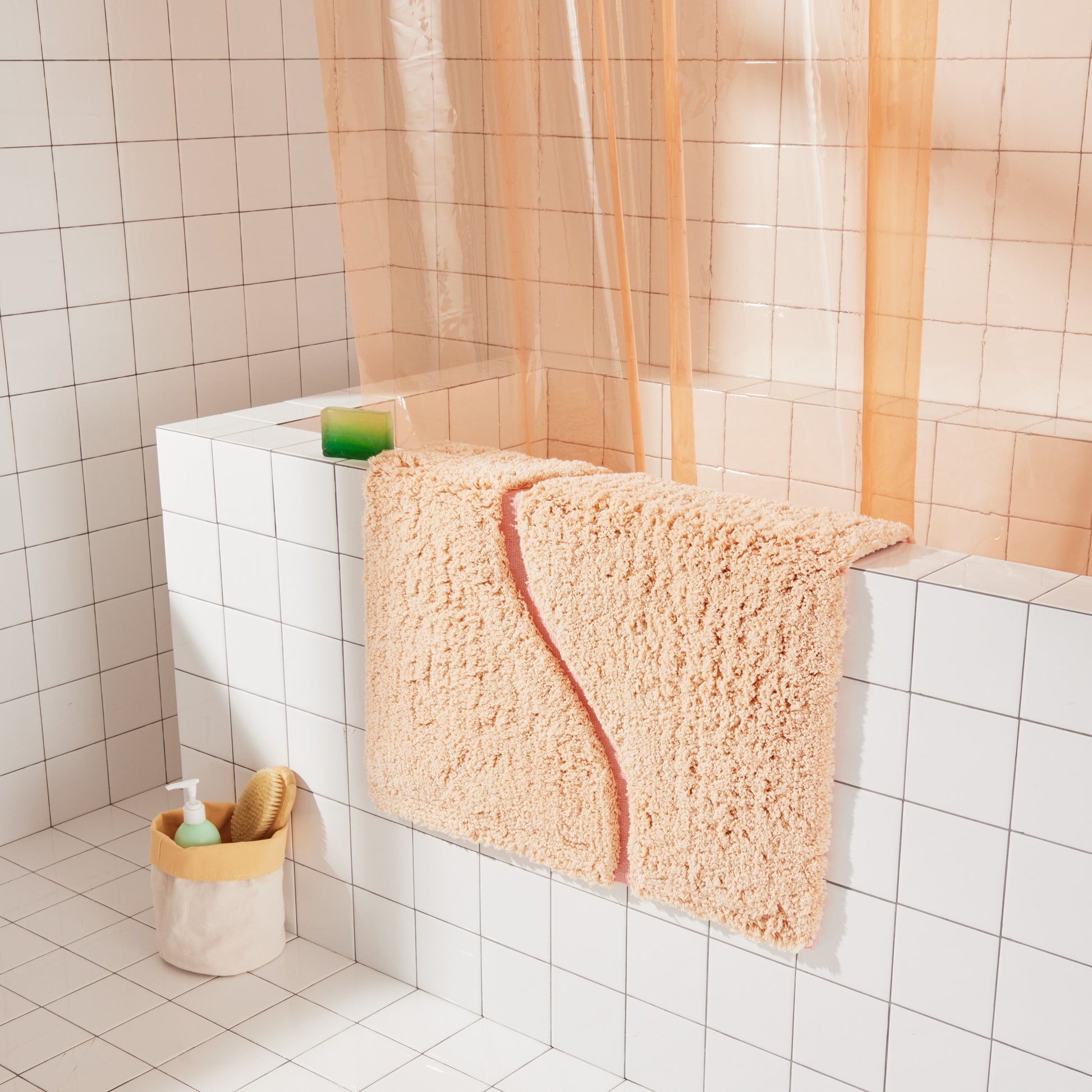 Peach bath mat in 21"x31" size with pink curvy path stripe contrast shot laid over the side of white tiled bathtub.