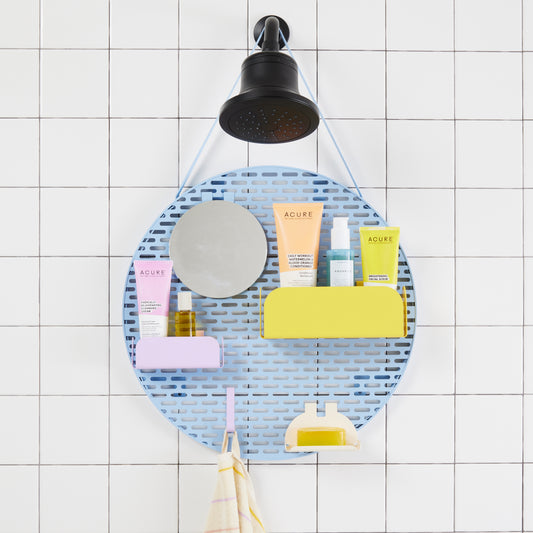 Circular blue shower organizer with modular shelving holding shower products strapped over shower head against a white tiled bathroom.