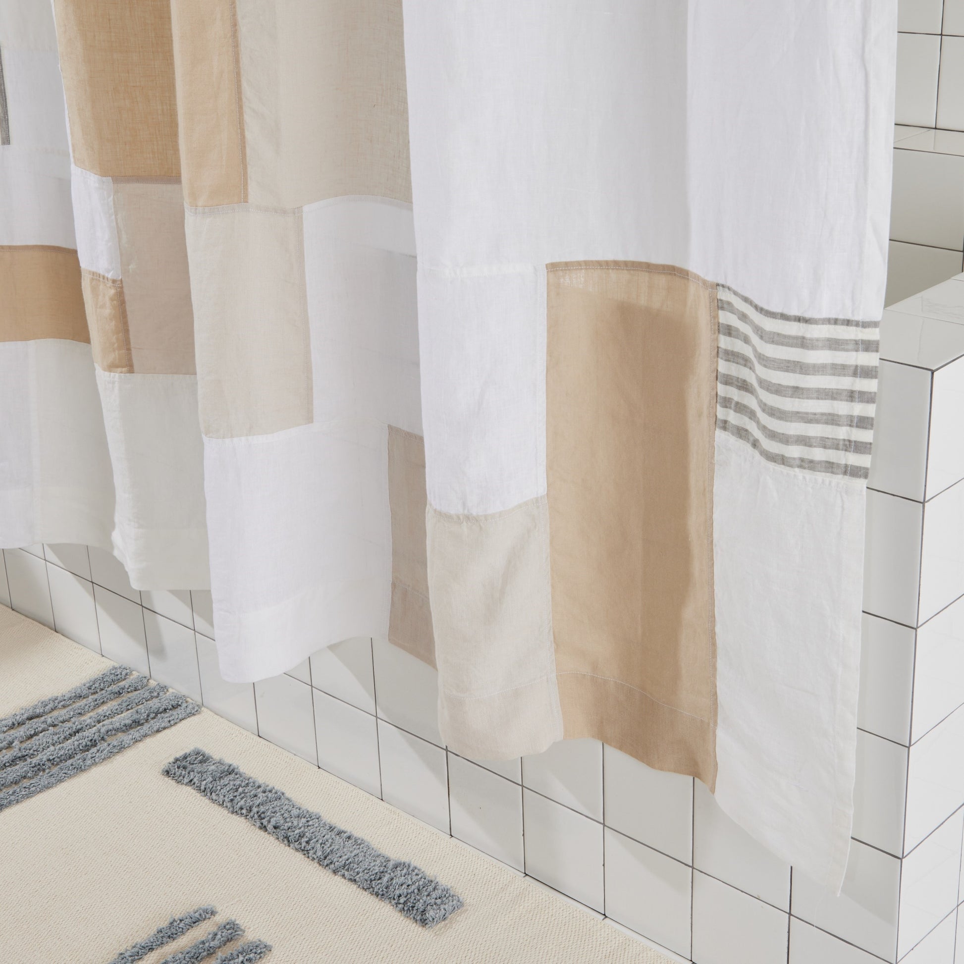 Bottom view of multi color linen shower curtain in sand hangs above reyes bath mat in storm.