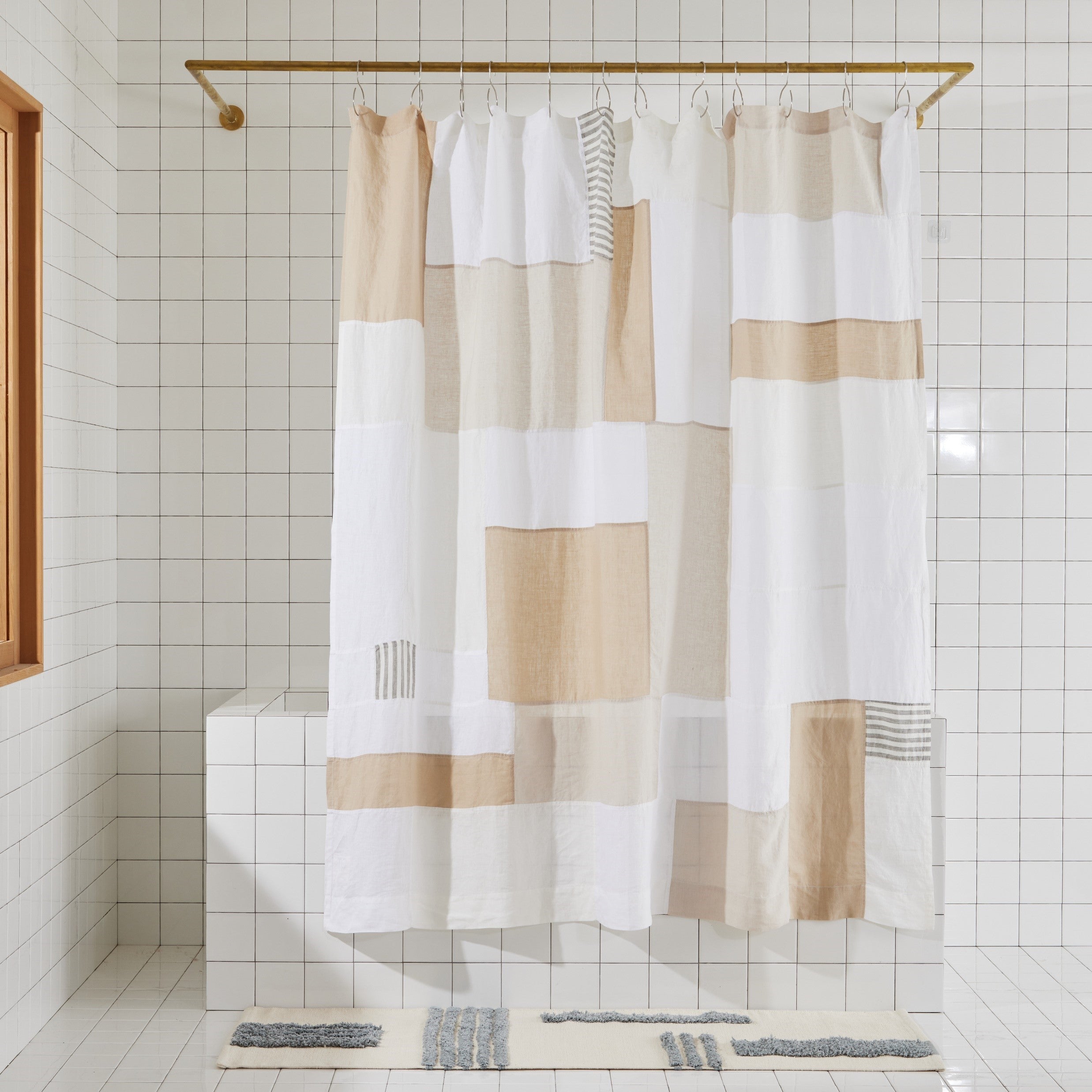 Multi-color cream and beige linen shower curtain hanging in white tiled bathroom.