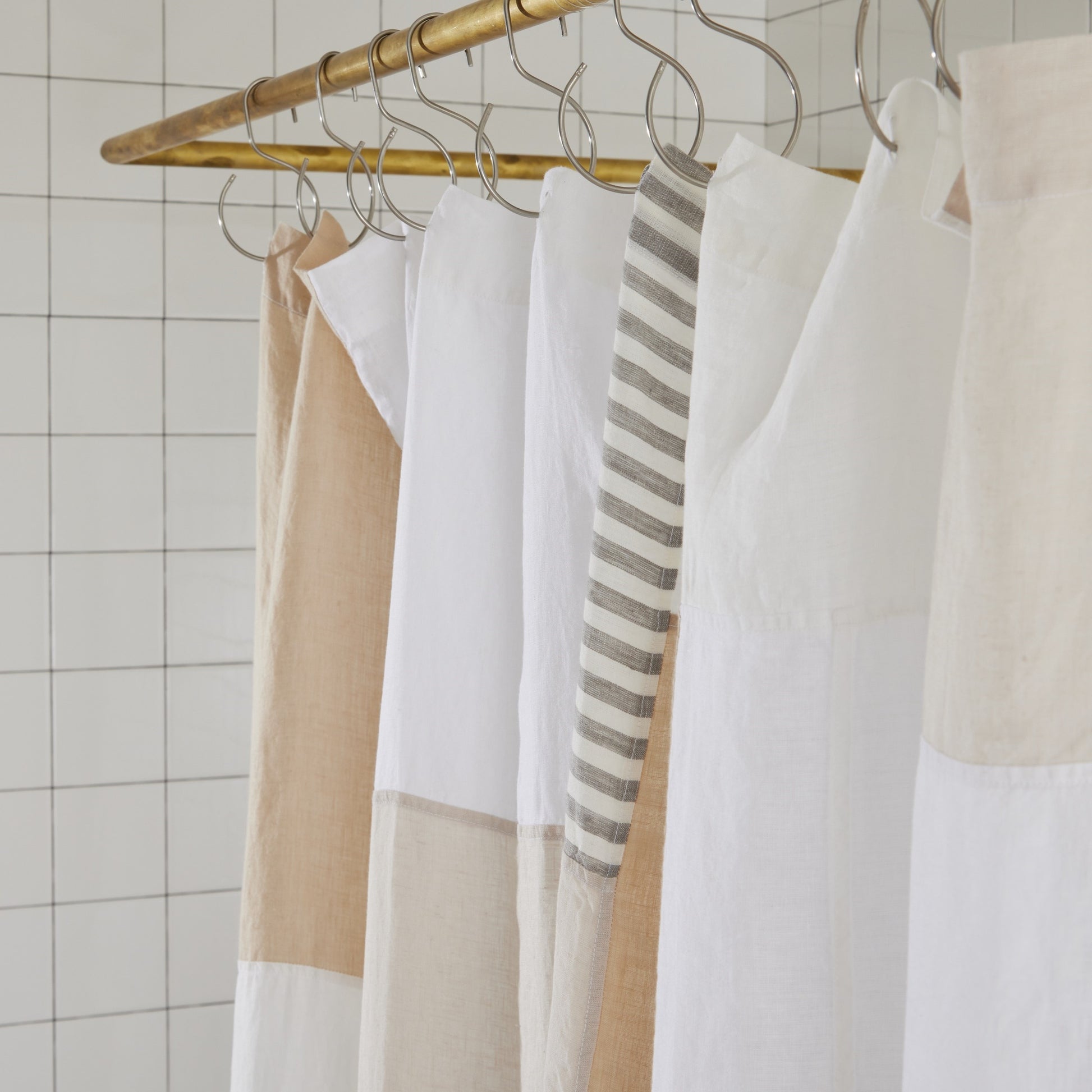 Top seam of multi-colored cream linen shower curtain hanging on brass rod with silver S hooks.