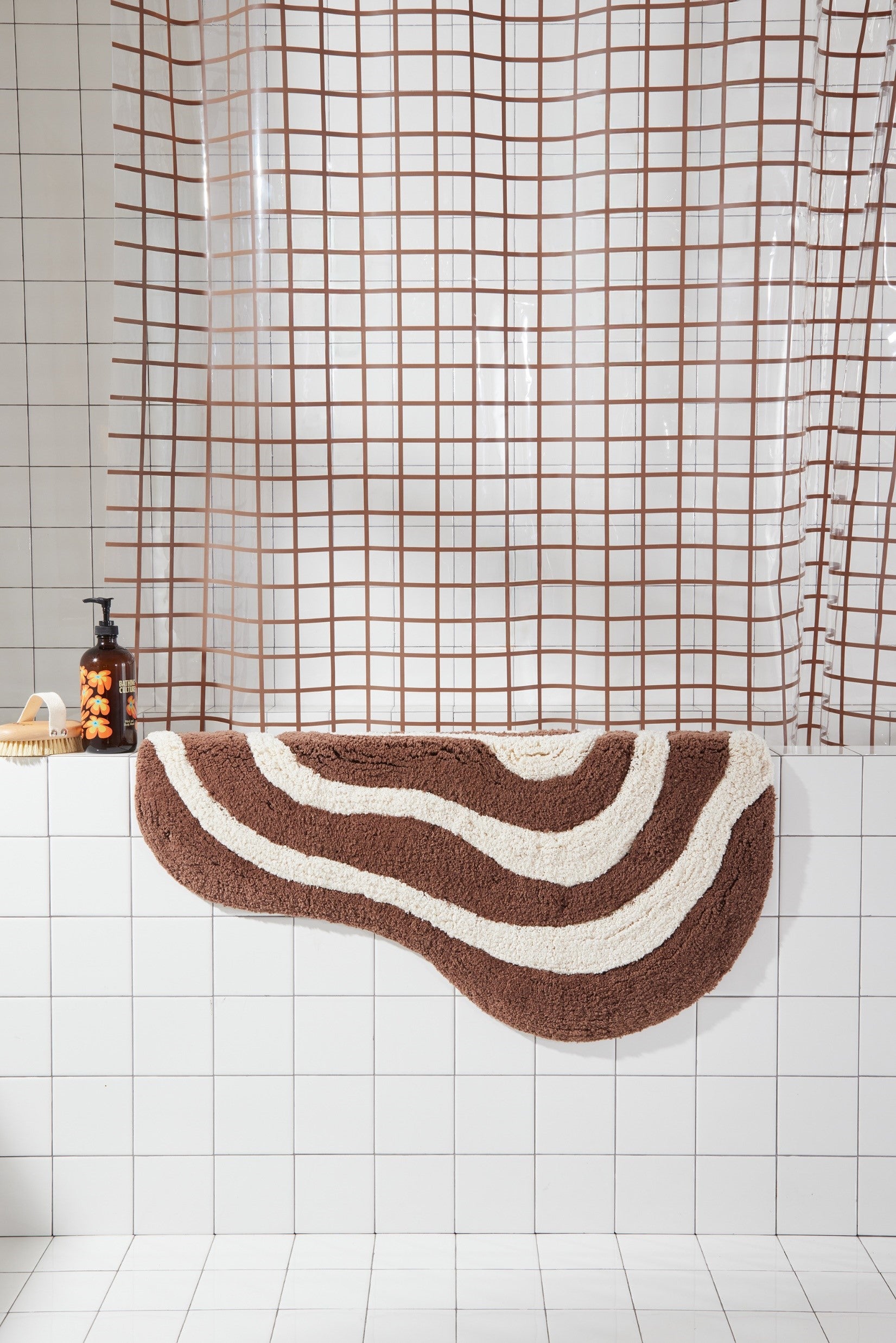 Brown and cream bath mat hanging over side of white tiled bathtub styled with 2x2 sun shower in chocolate.
