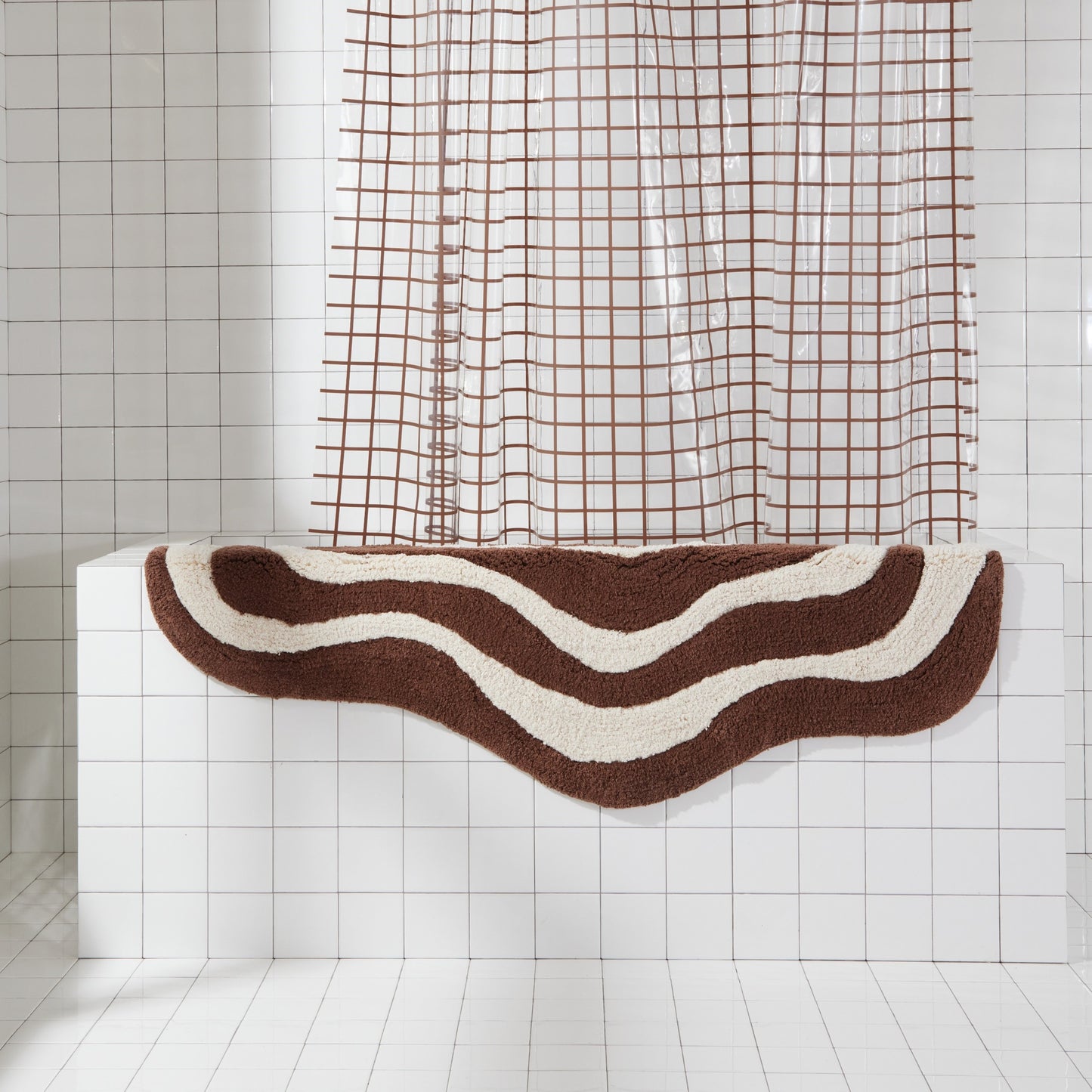 Wave shaped brown and cream striped bath mat runner in 56"x22" size hanging over side of white tiled bathtub.