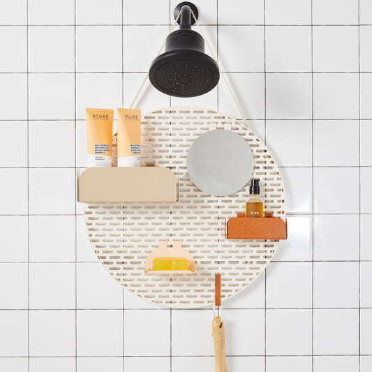 The Spot in "sand" cream colored on white tile background hanging from a black shower head.