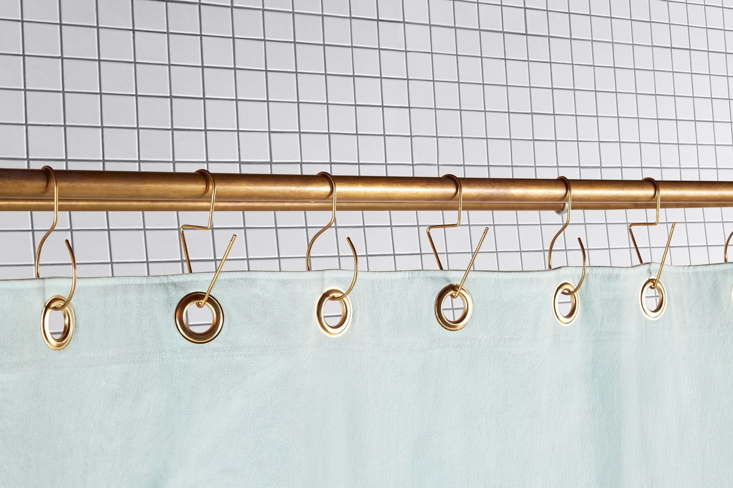 mint green curtain with brass grommets hanging from brass hooks
