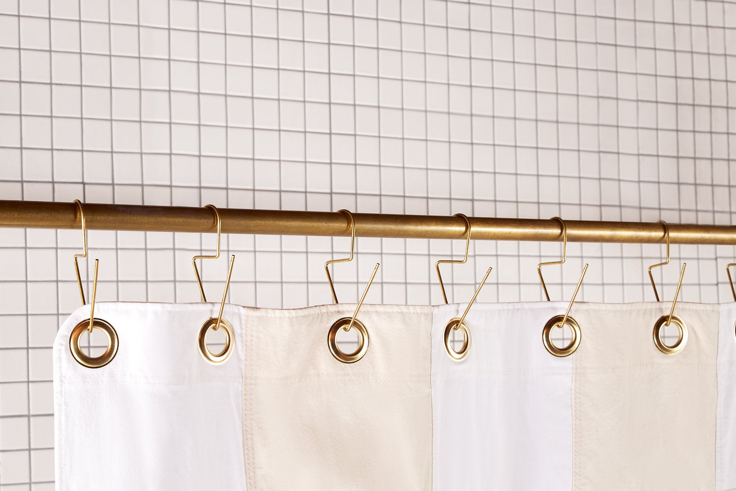 Re:Canvas Checker Sand detail view of grommets and hooks hanging from shower curtain rod.