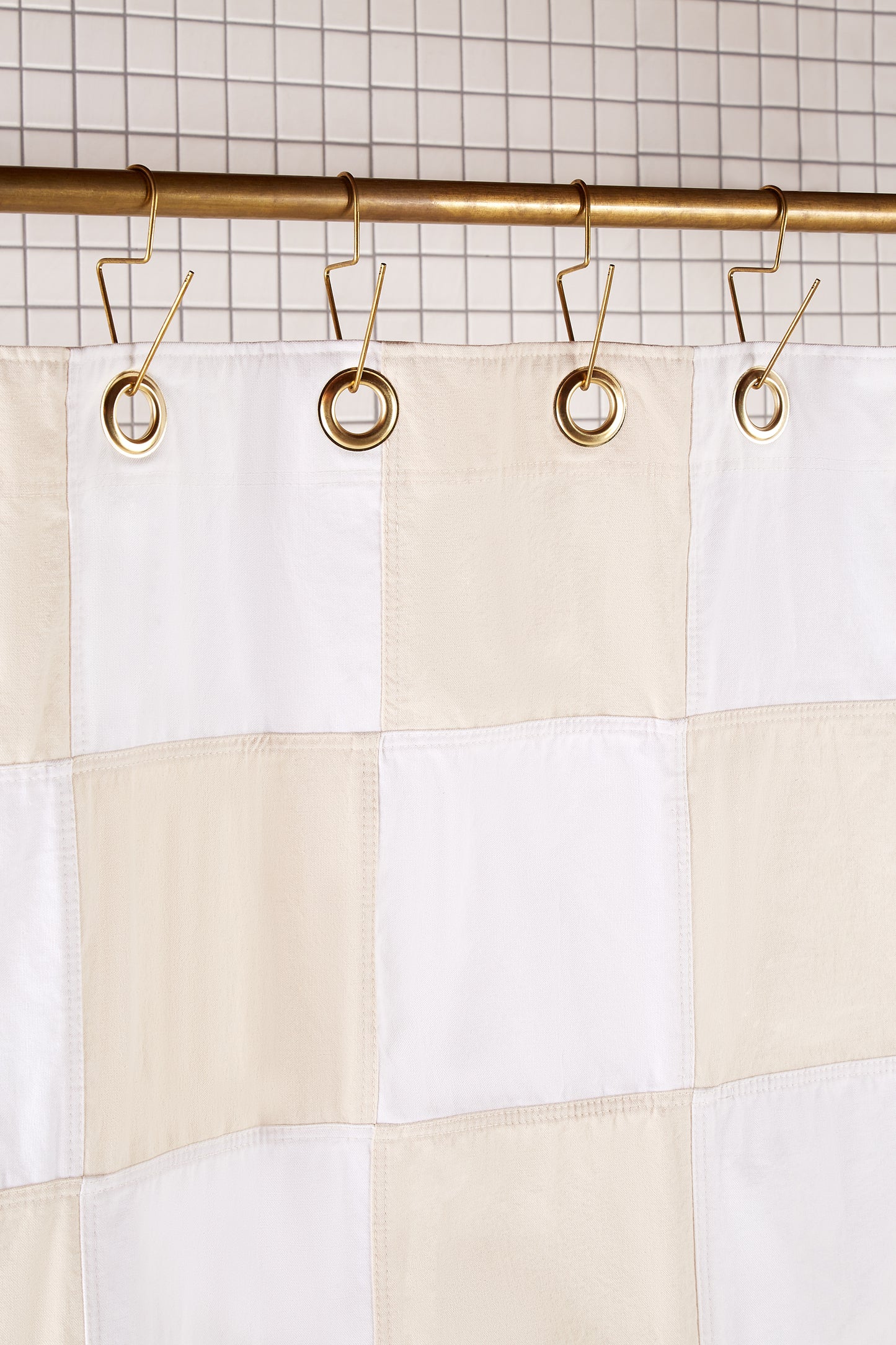 Re:Canvas Checker Sand detail view of grommets and hooks hanging from shower curtain rod.