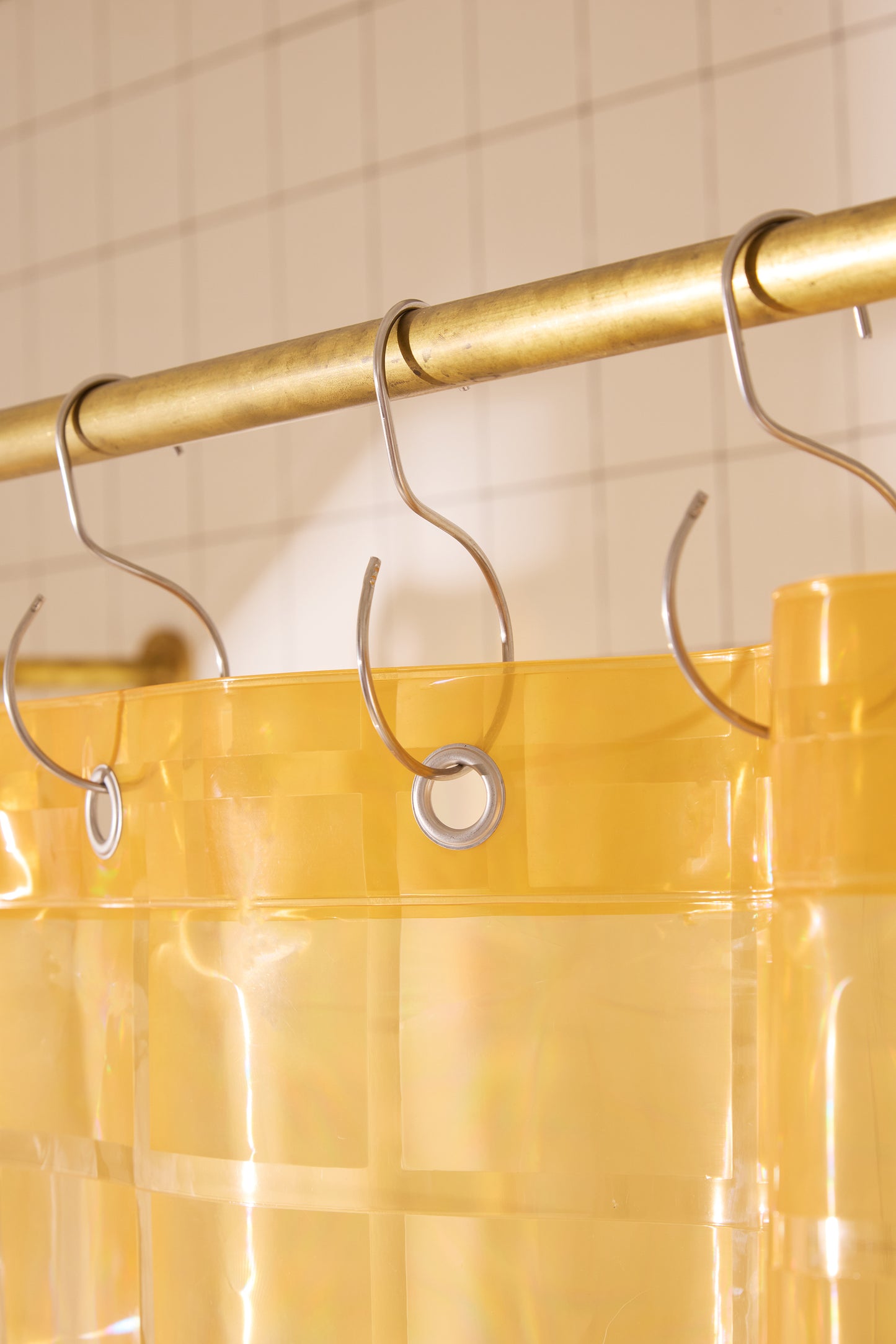 Yellow shower curtain with gold rod and clear hooks on a tiled wall background