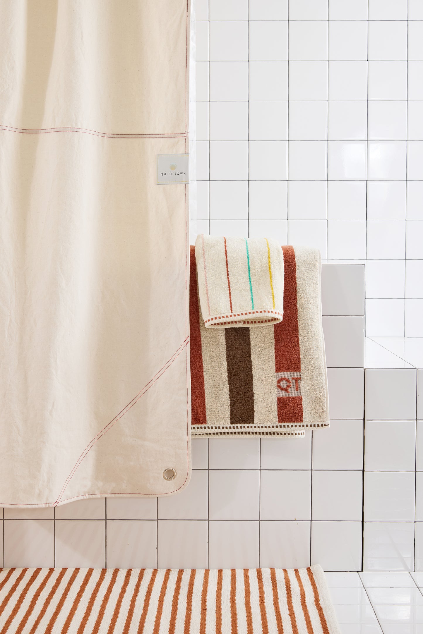 cream colored curtain with red stitching styled in white tiled bathroom with striped rug and towels. 
