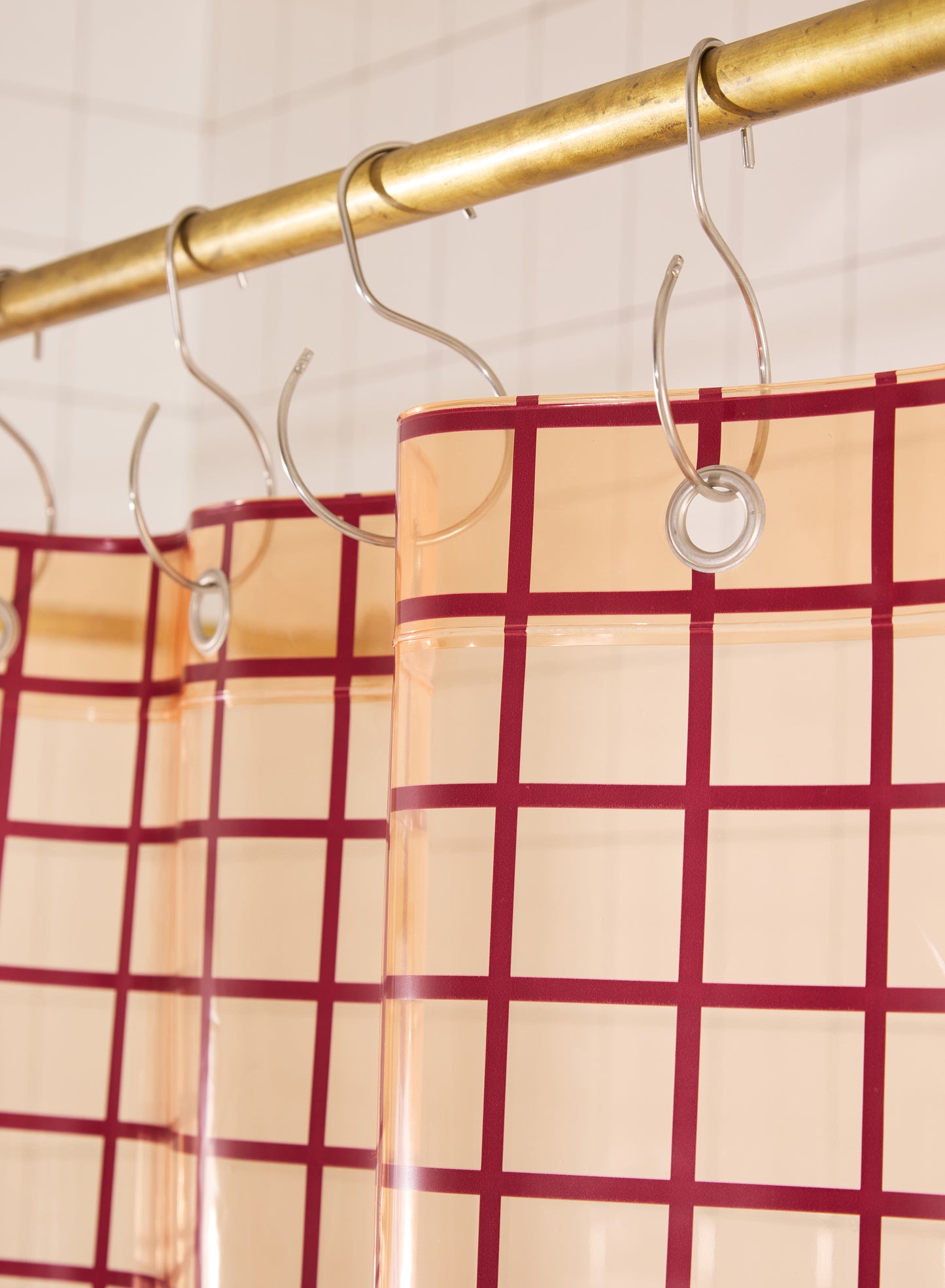 Red and peach checkered curtain with silver hooks on a gold rod.