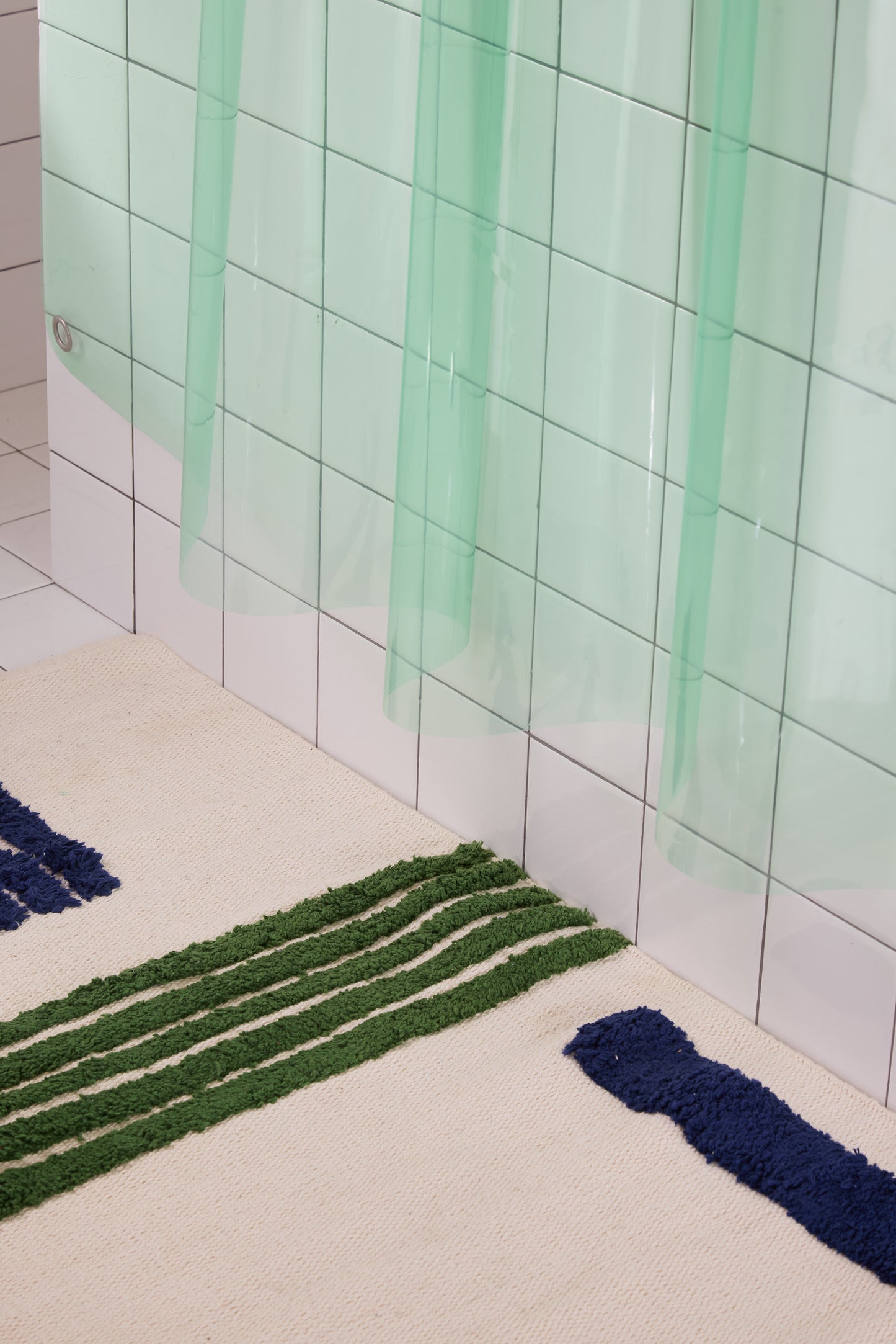 Bath mat with green and blue stripes on a tiled bathroom floor