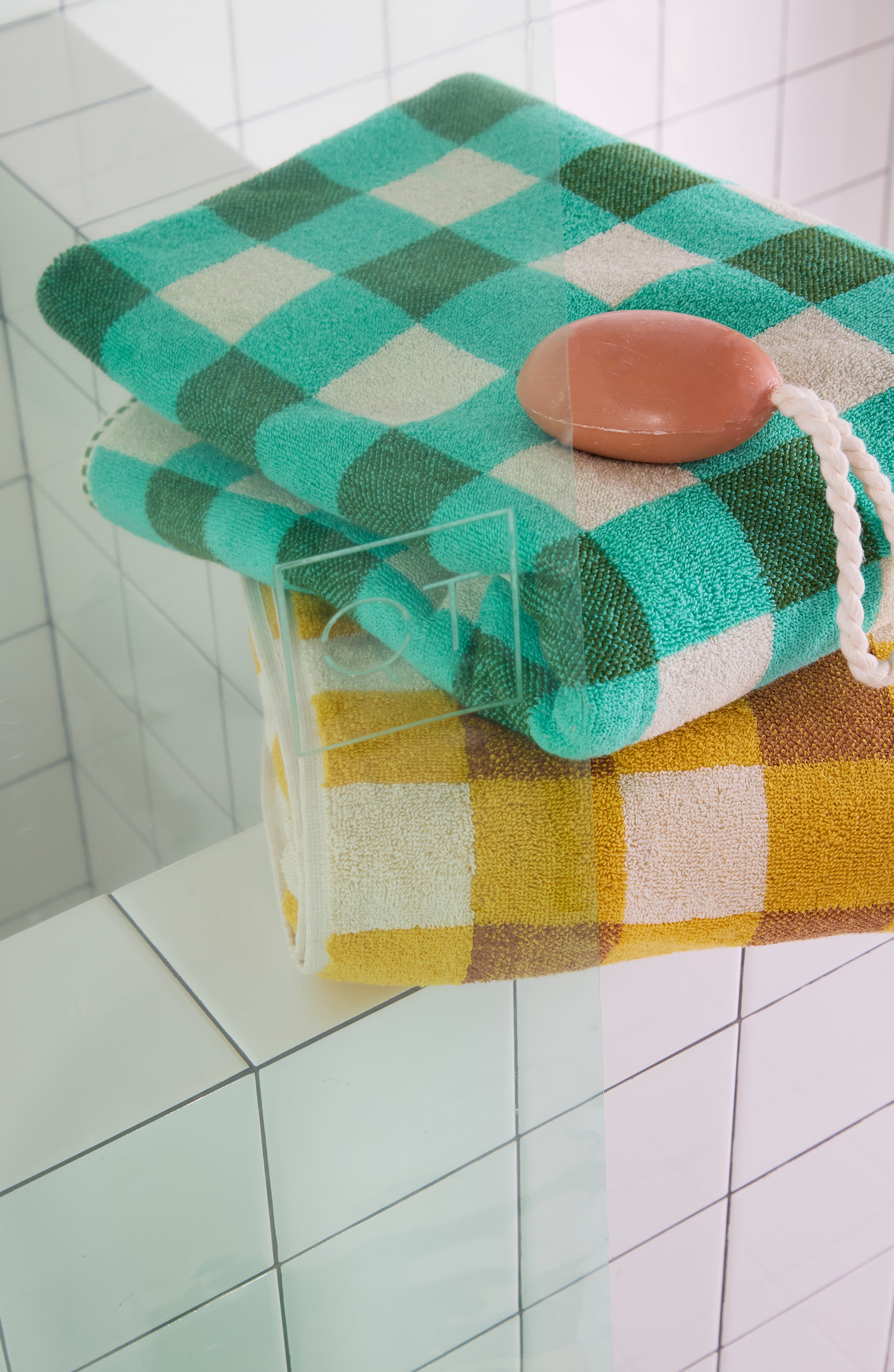 Checkered towel with a bar of soap on a tiled bathroom shelf with mint green clear shower curtain