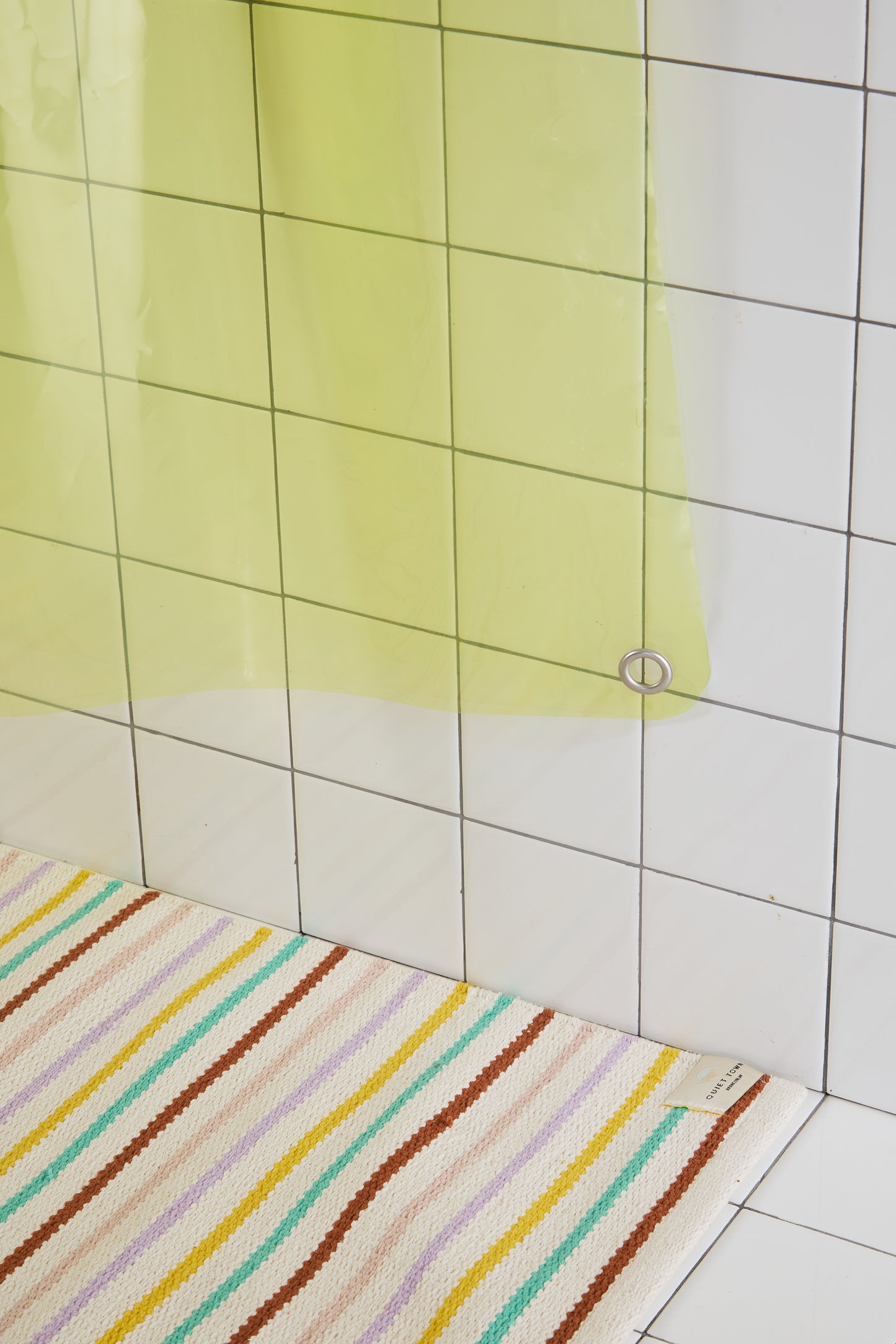 Striped bath mat on a tiled bathroom floor with a yellow shower curtain.