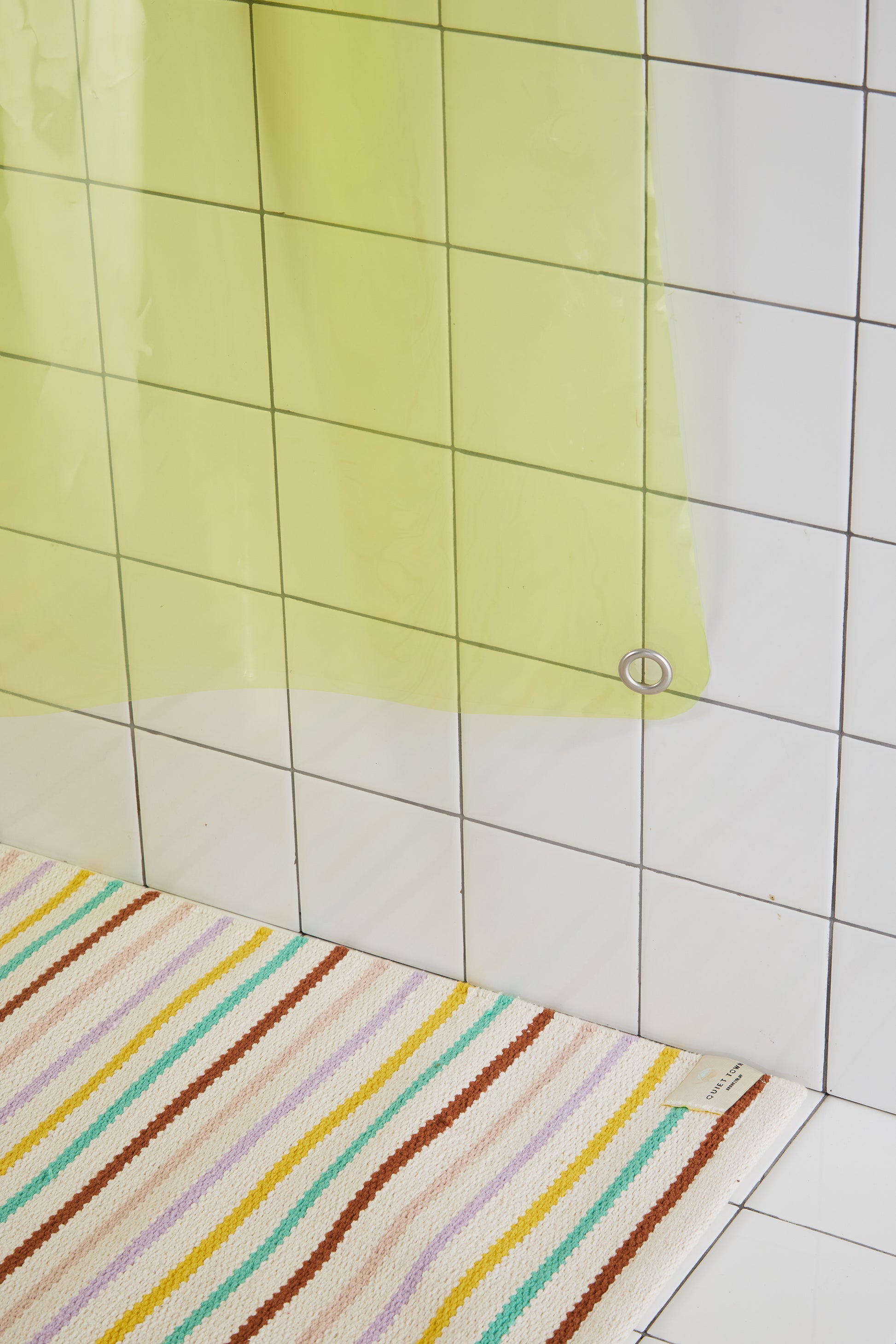 Striped bath mat on a tiled bathroom floor with a yellow shower curtain.