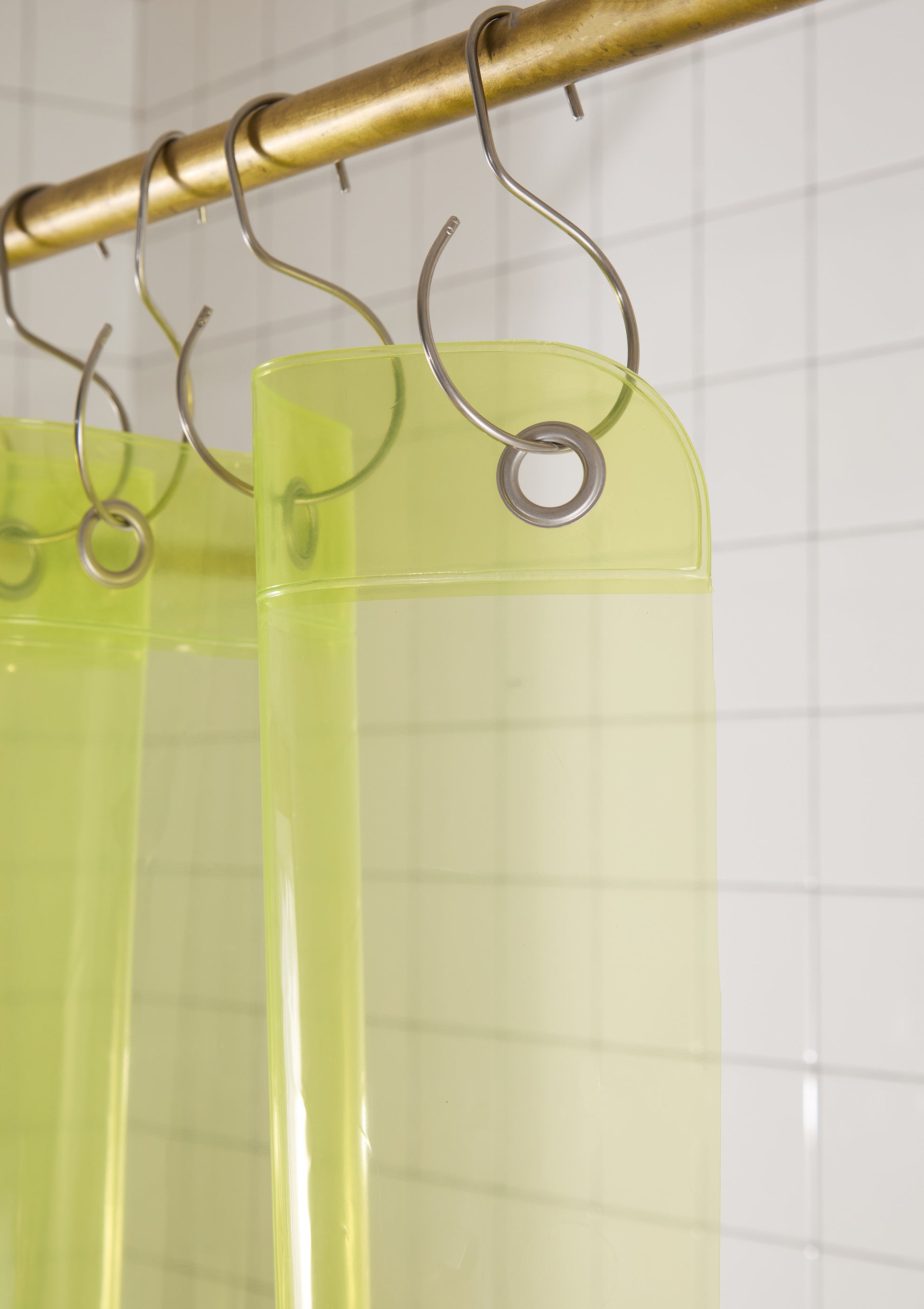 Clear shower curtain with gold rod and silver hooks on a tiled bathroom wall.