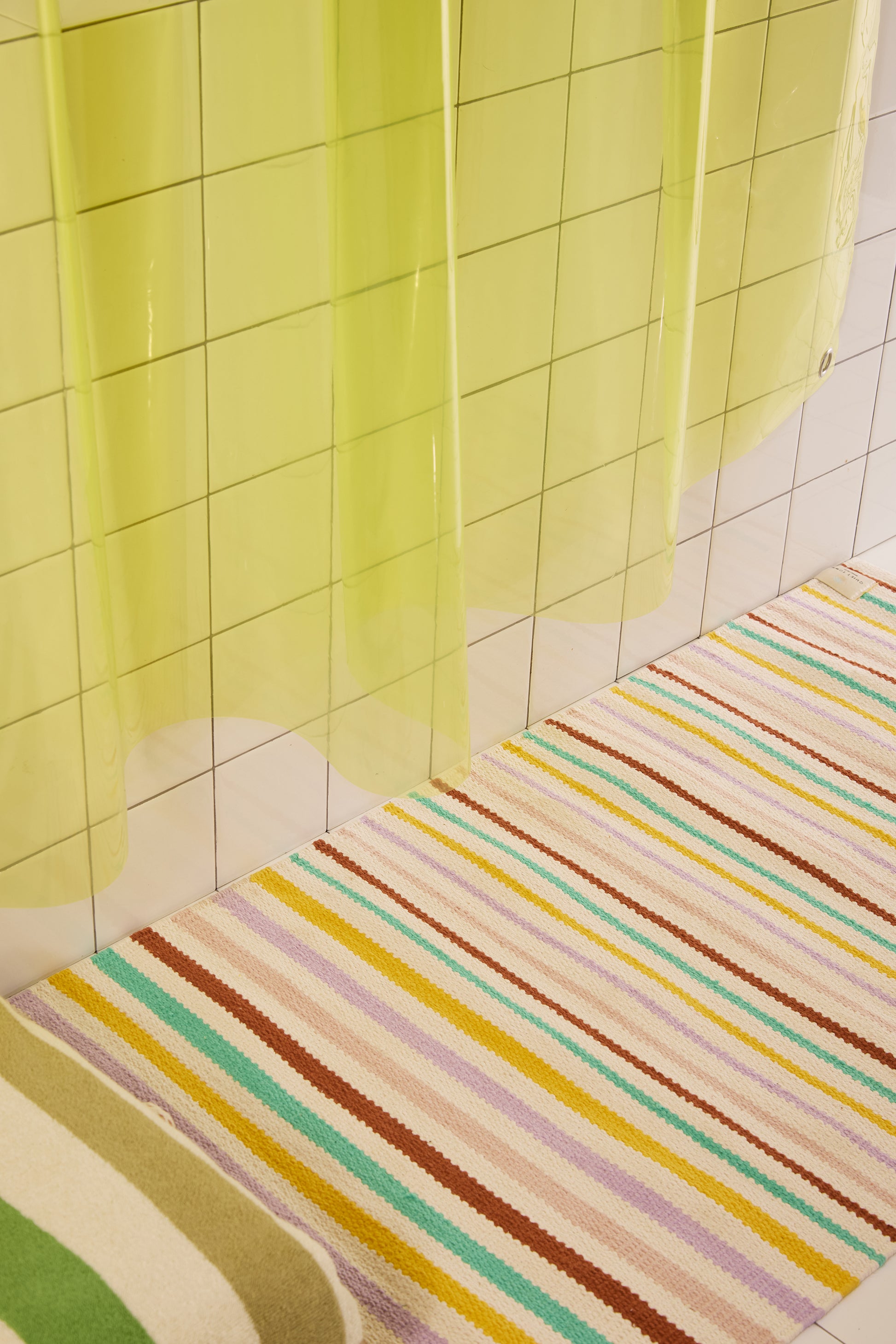 Colorful striped rug on a tiled bathroom floor with a green shower curtain.