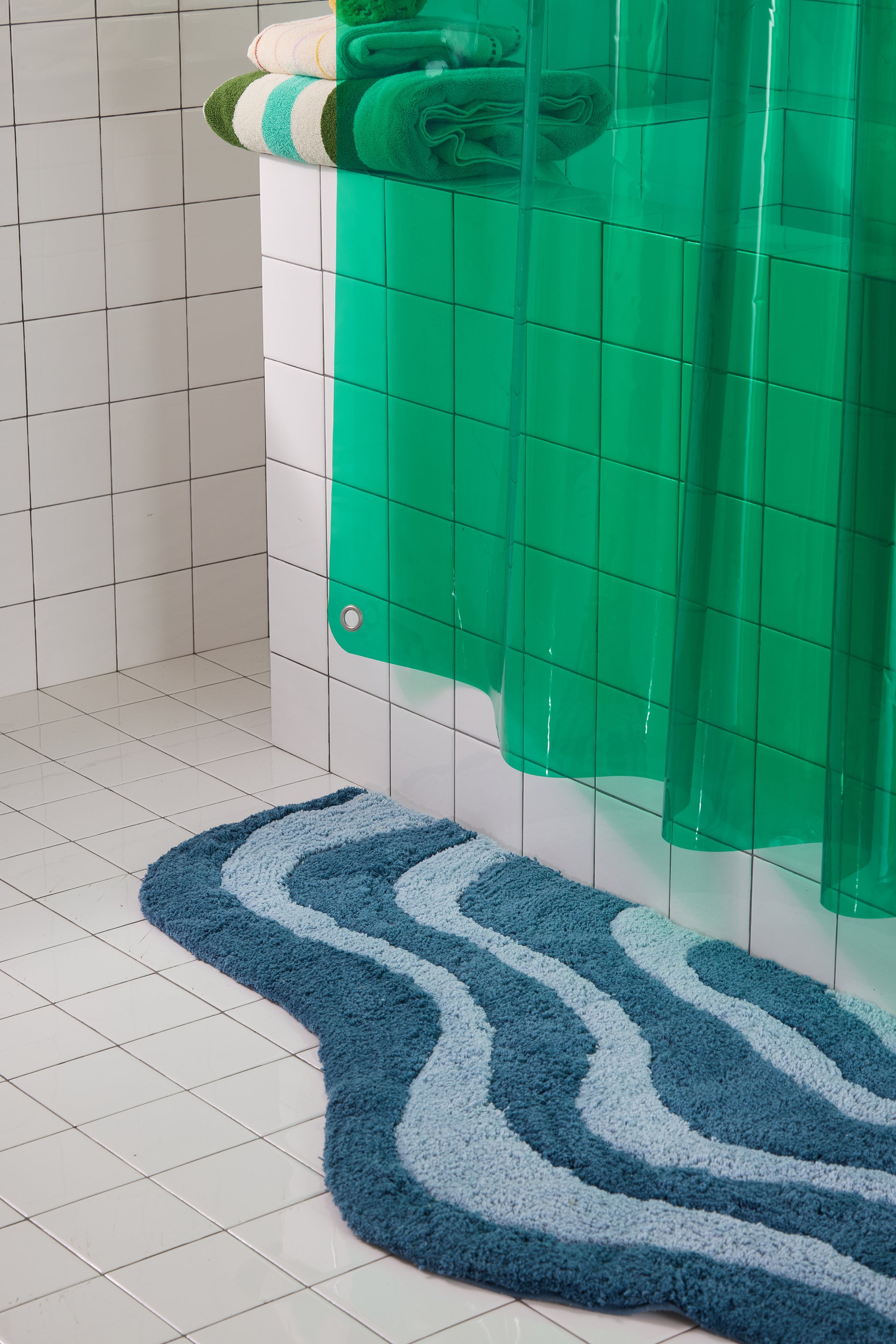 Bathroom with a green shower curtain and blue textured rug on a tiled floor.