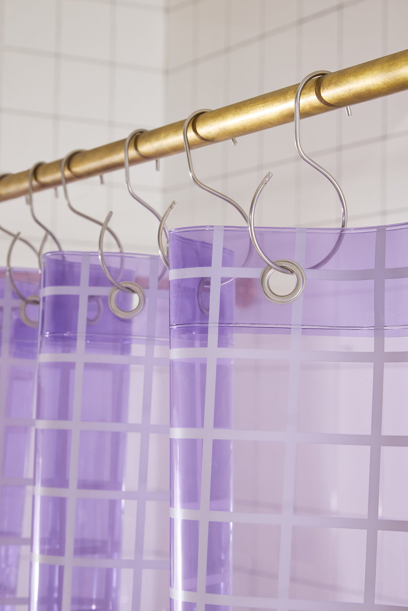 Purple shower curtain with gold hooks on a tiled bathroom wall.