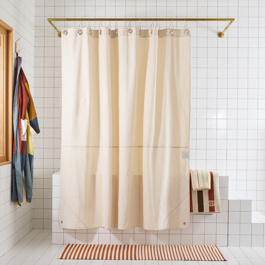 cream colored curtain hanging in white tiled bathroom with striped rug and striped towels.