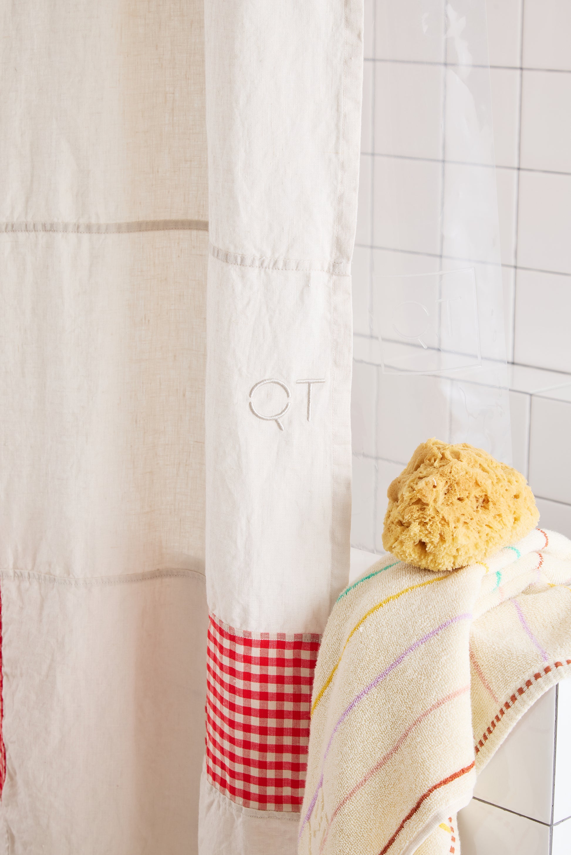 White shower curtain with red checkered trim and a sponge on a tiled bathroom wall.