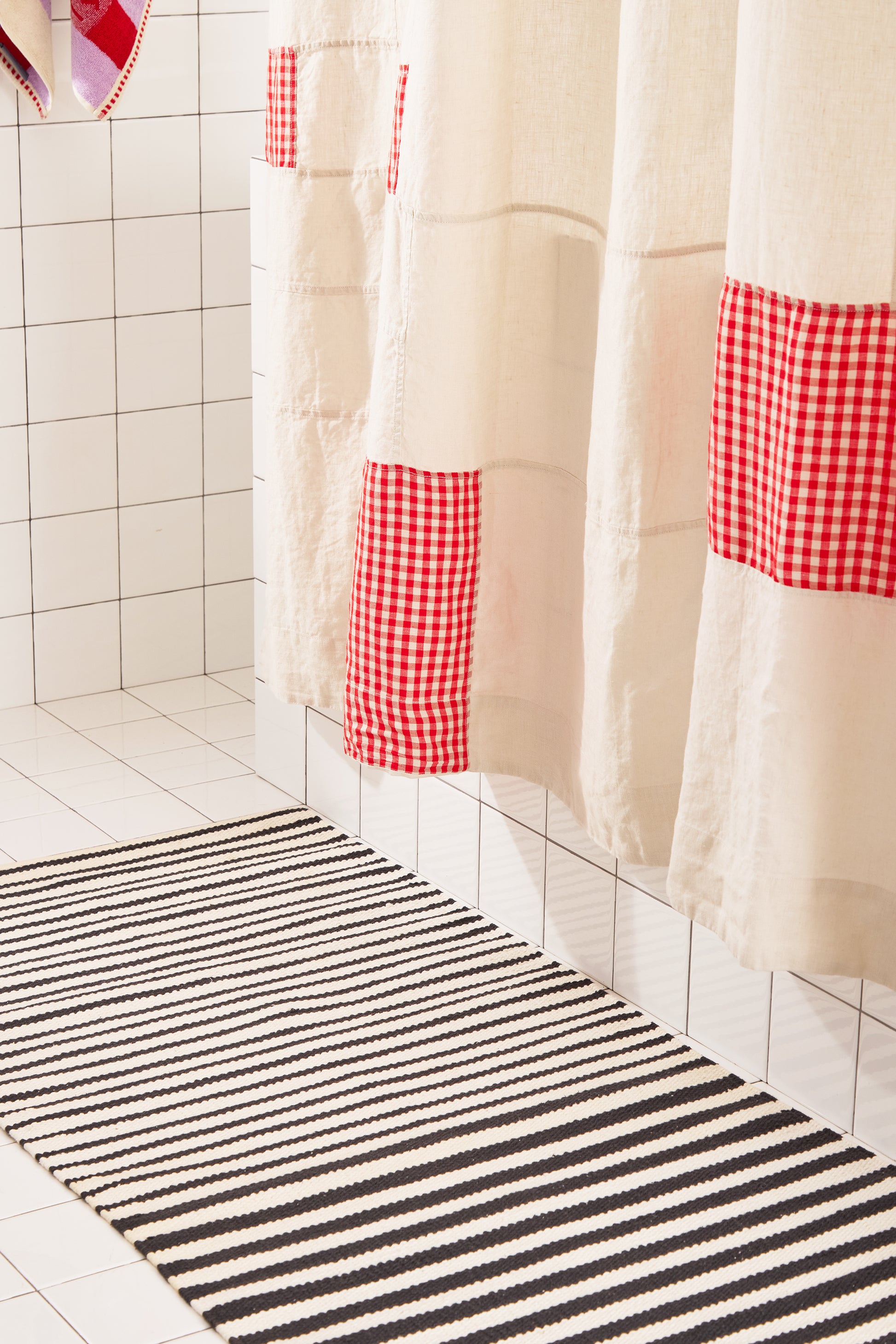 Striped bath mat in front of a shower with a checkered curtain