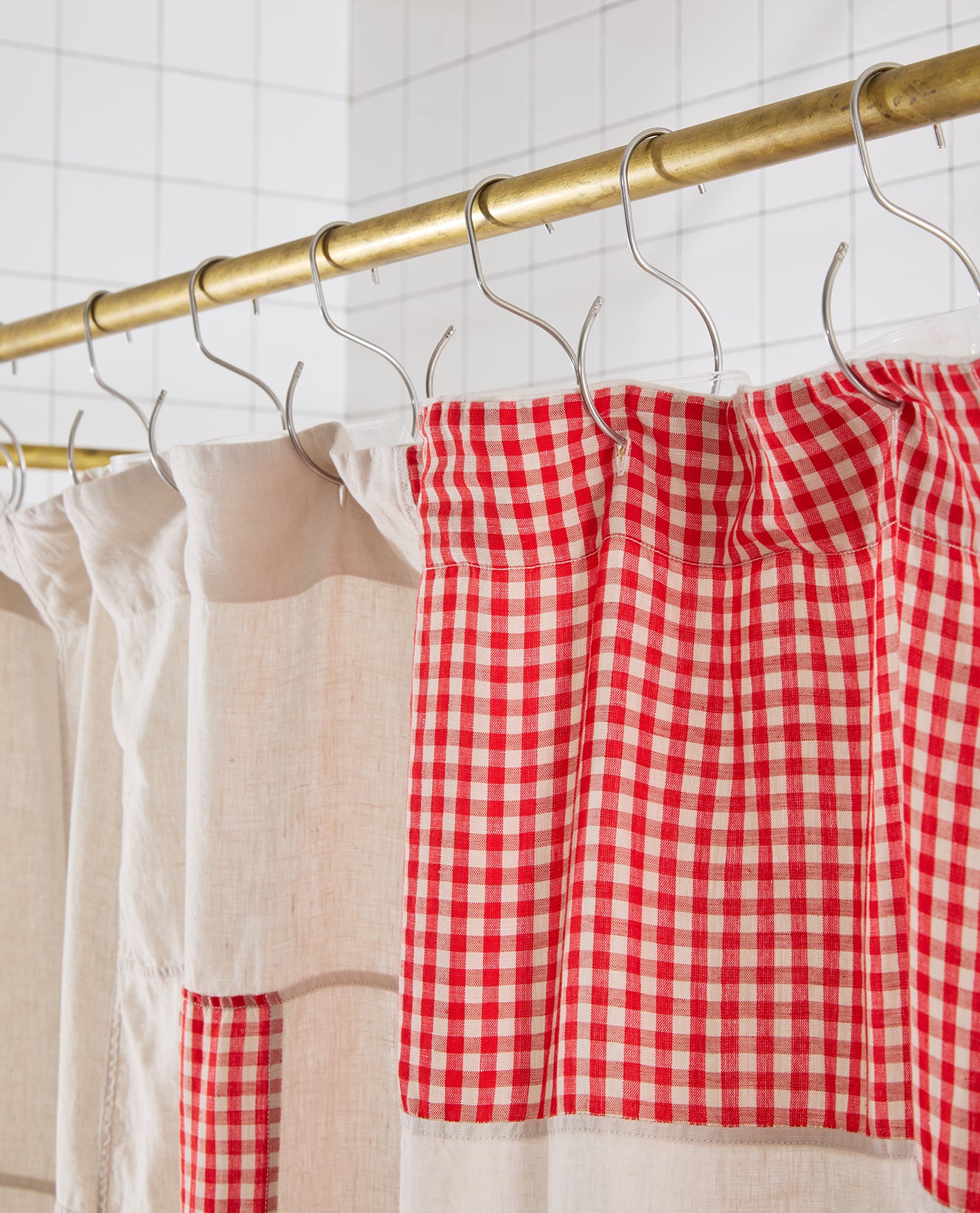 Red and white checkered shower curtain hanging on a gold rod with a tiled wall background