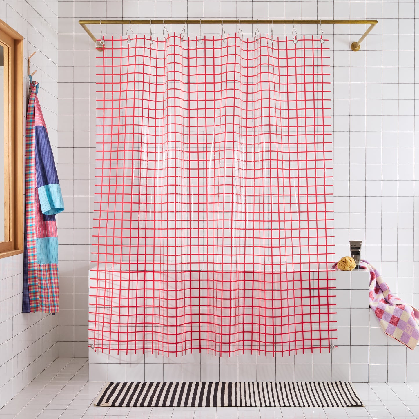 Bathroom with a red grid-patterned shower curtain, colorful towels, and a striped rug.