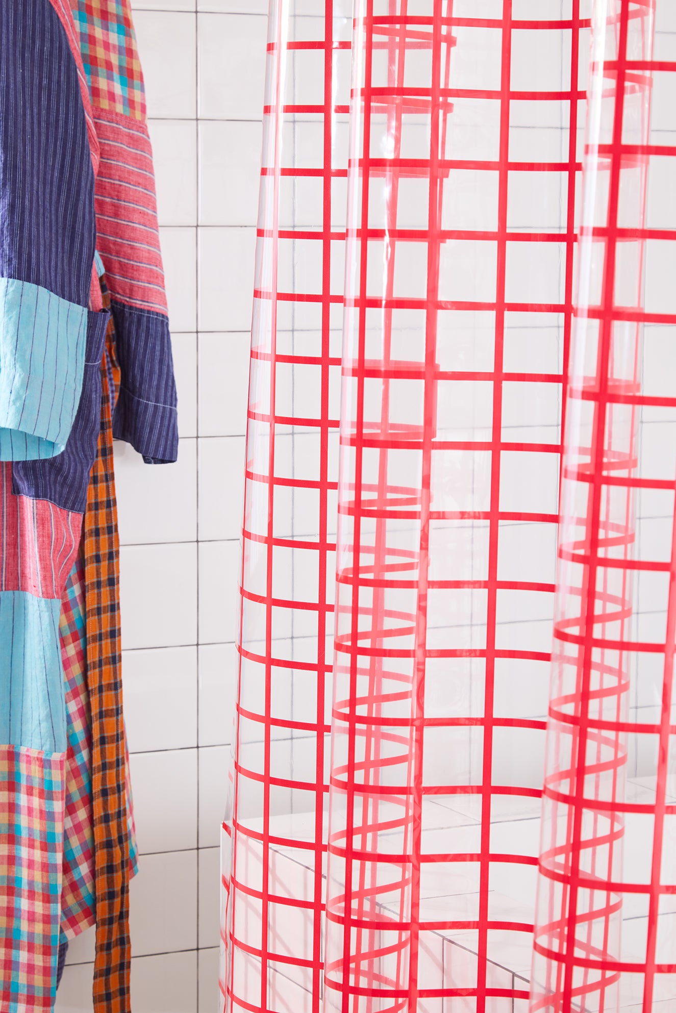 Red grid-patterned shower curtain with colorful robe hanging against a tiled wall.