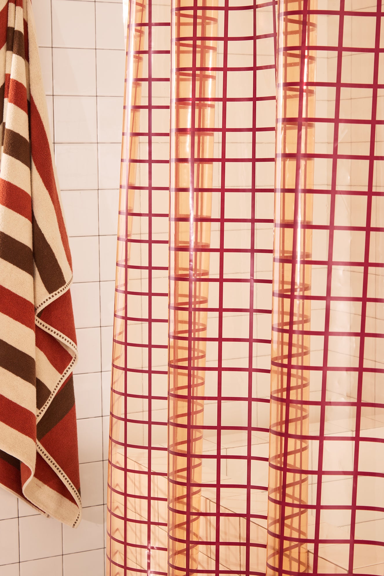 checkered shower curtain on a tiled bathroom wall with a striped towel.