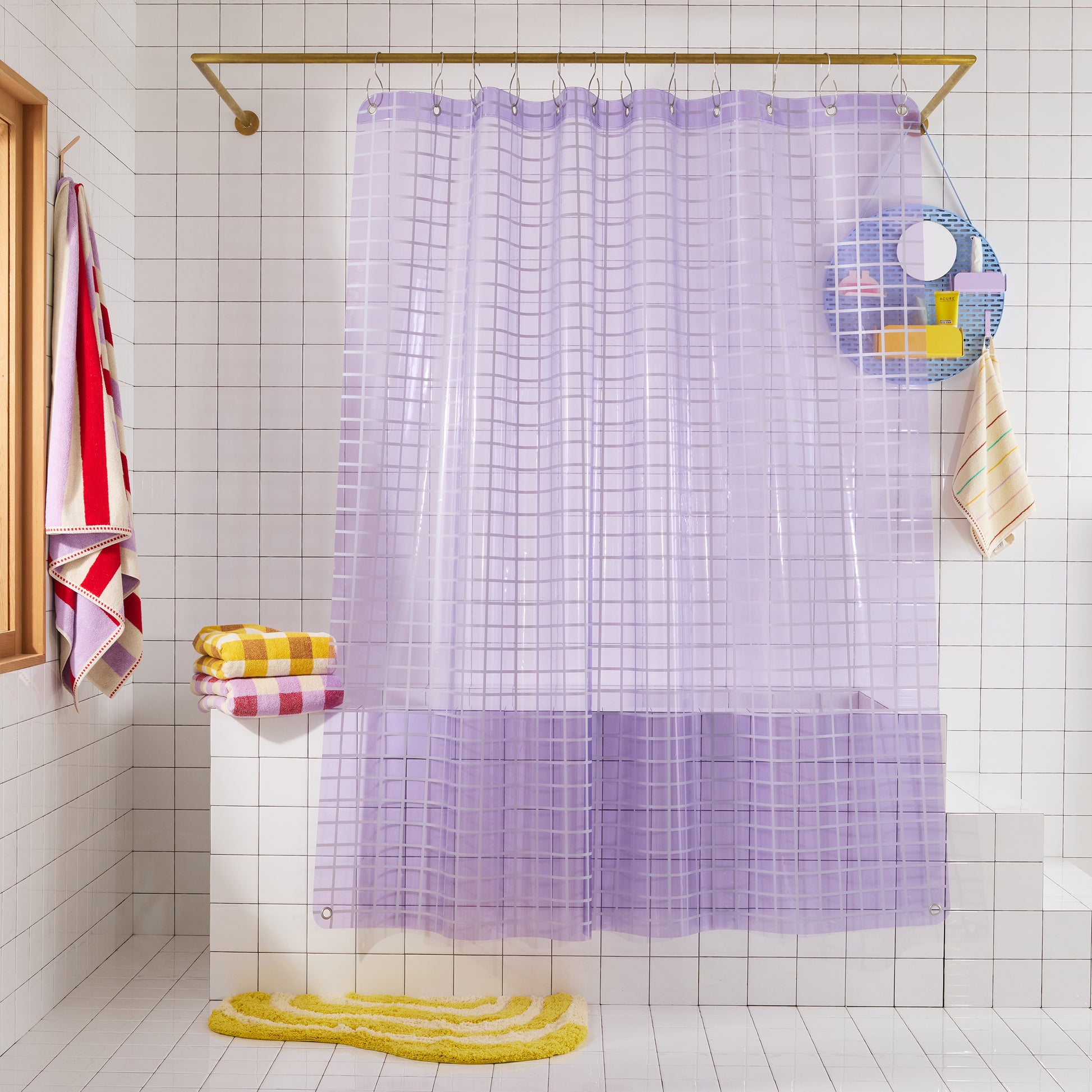 Lavender grid-patterned shower curtain in a bathroom with tiled walls and colorful towels.