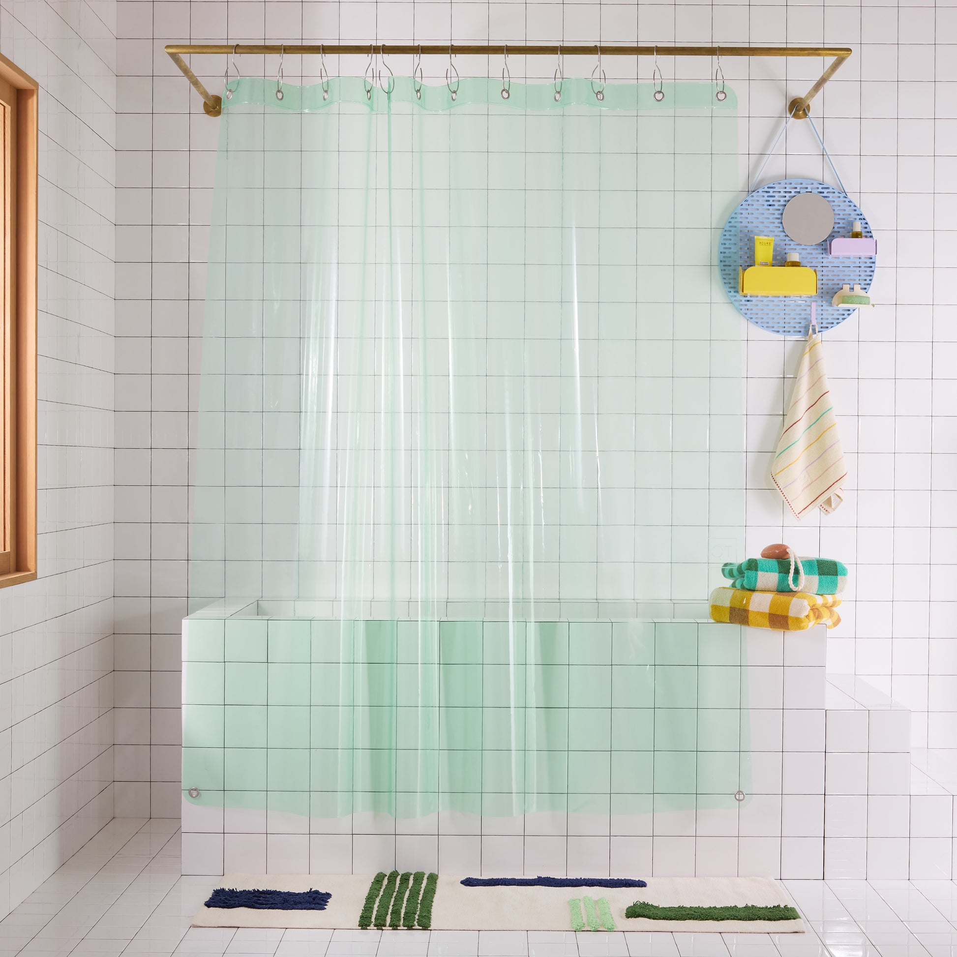 Bathroom with a mint green clear shower curtain, colorful bath toys, and towels.