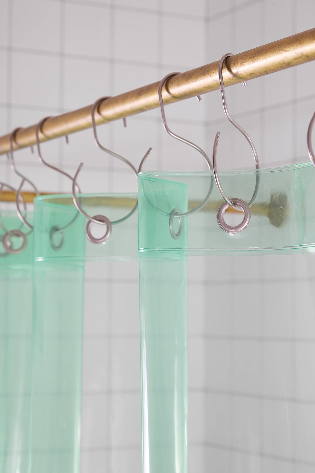 Green shower curtain with metal hooks on a gold rod against a tiled wall.