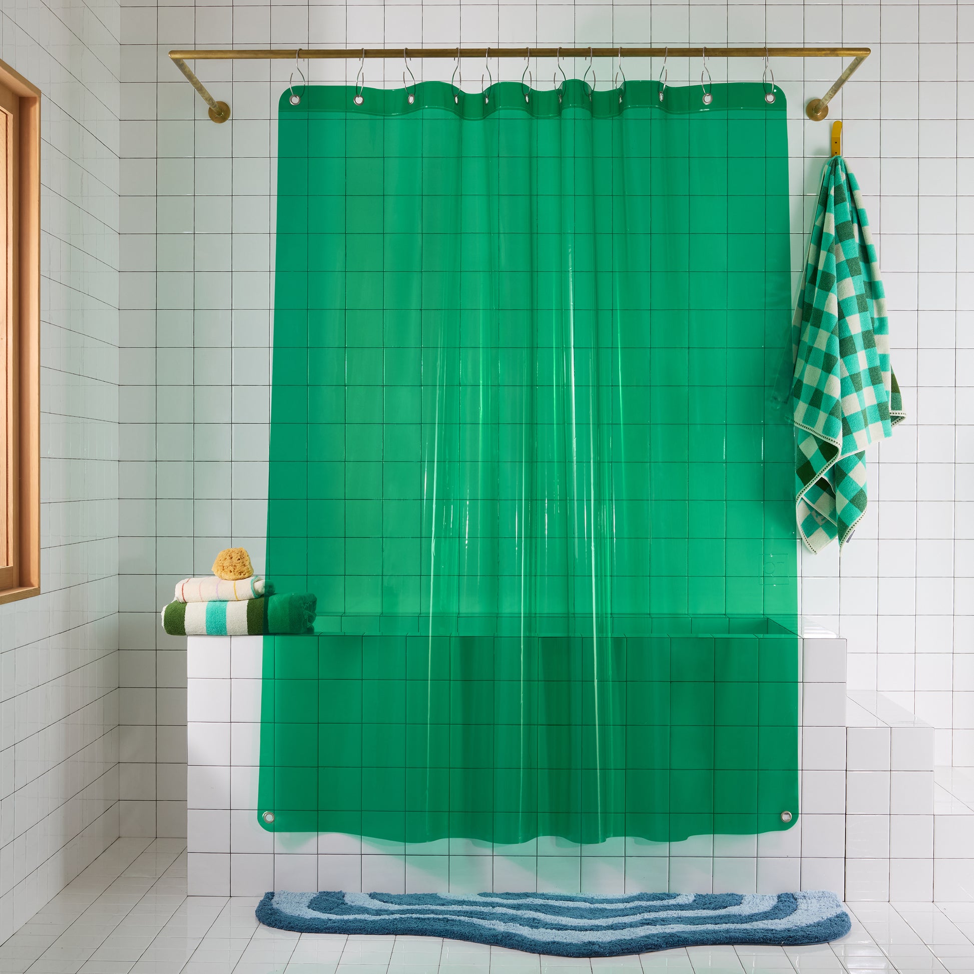 Green shower curtain with a checkered towel hanging on a hook in a bathroom.