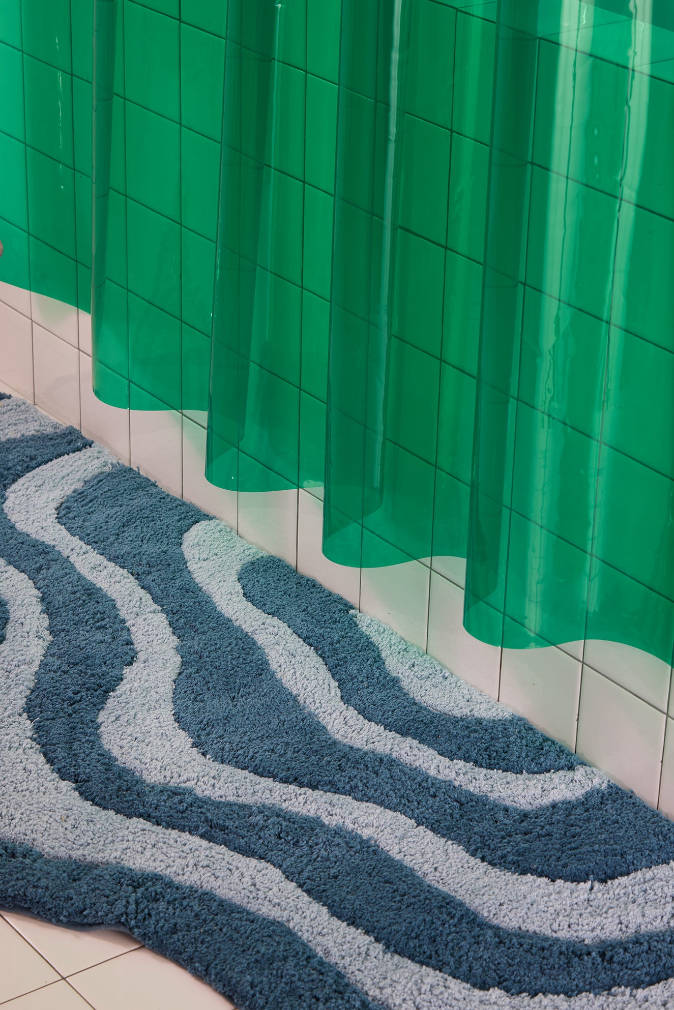 Blue textured bath mat on a tiled bathroom floor with a green shower curtain.