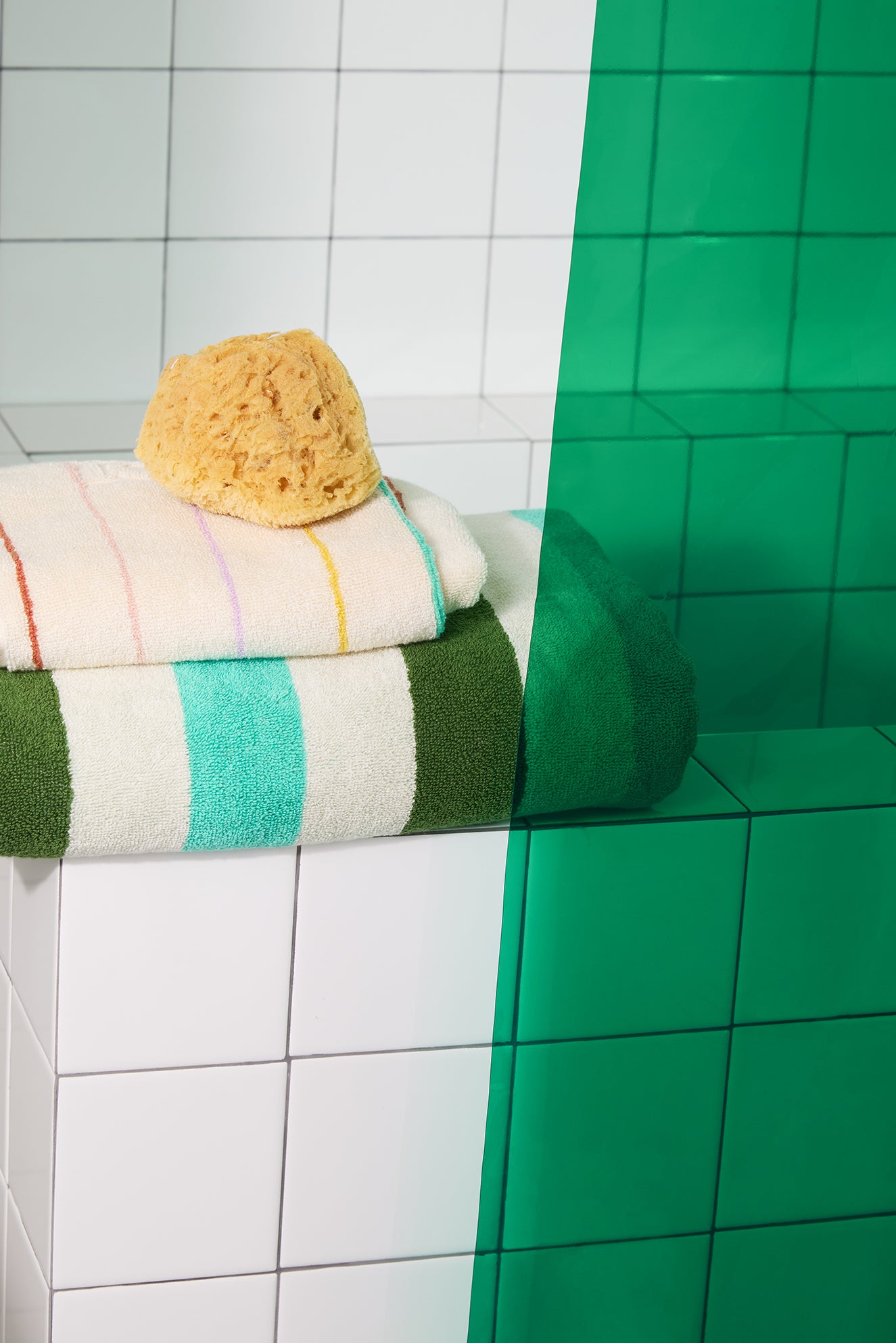 Towel with a sponge on top of it next to green tiles in a bathroom setting