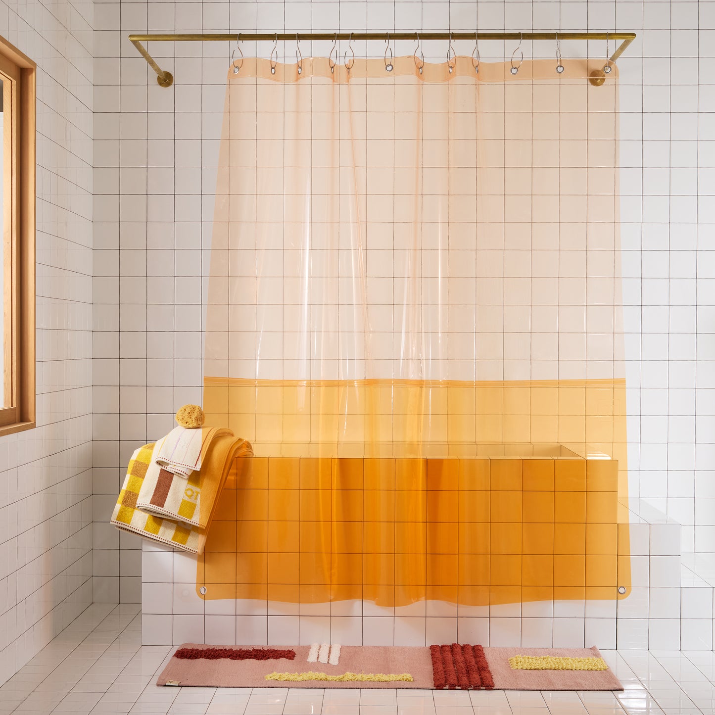 Bathroom with a peach and orange shower curtain, bath mat, and towel on a tiled wall.
