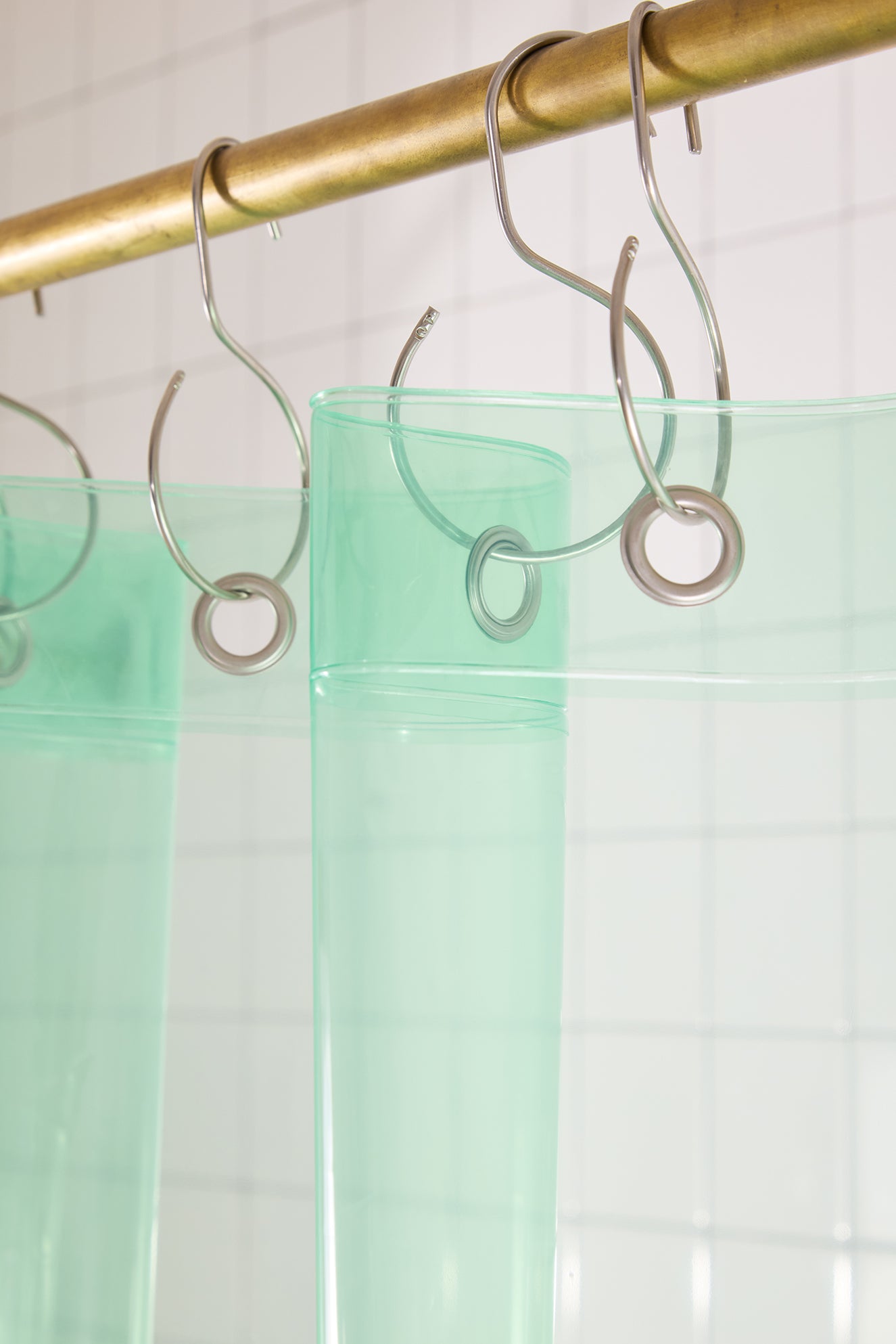Green shower curtain with silver hooks on a gold rod