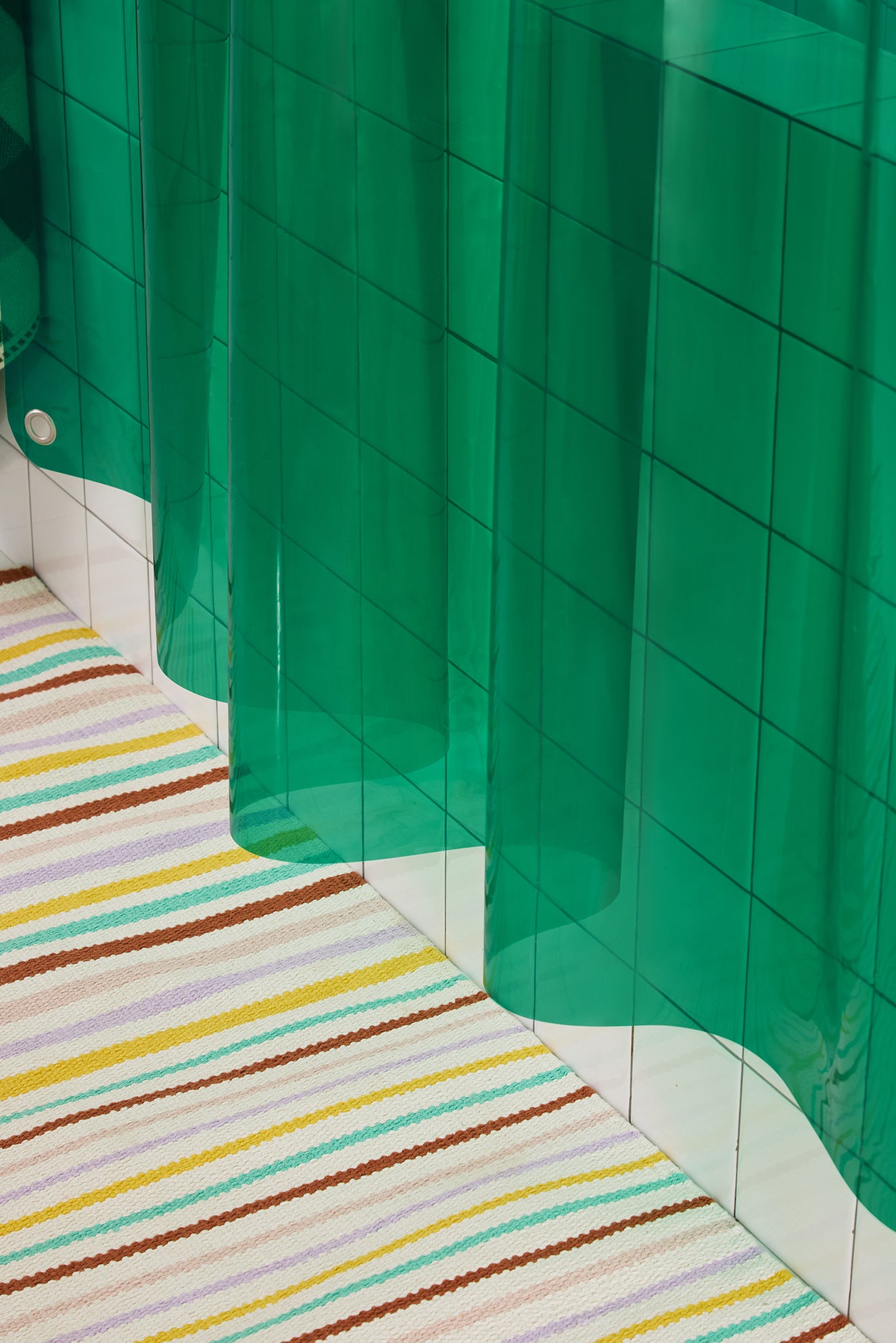 Green shower curtain with a colorful striped rug on a tiled floor