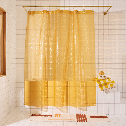 Yellow shower curtain in a bathroom with tiled walls and a bath mat.