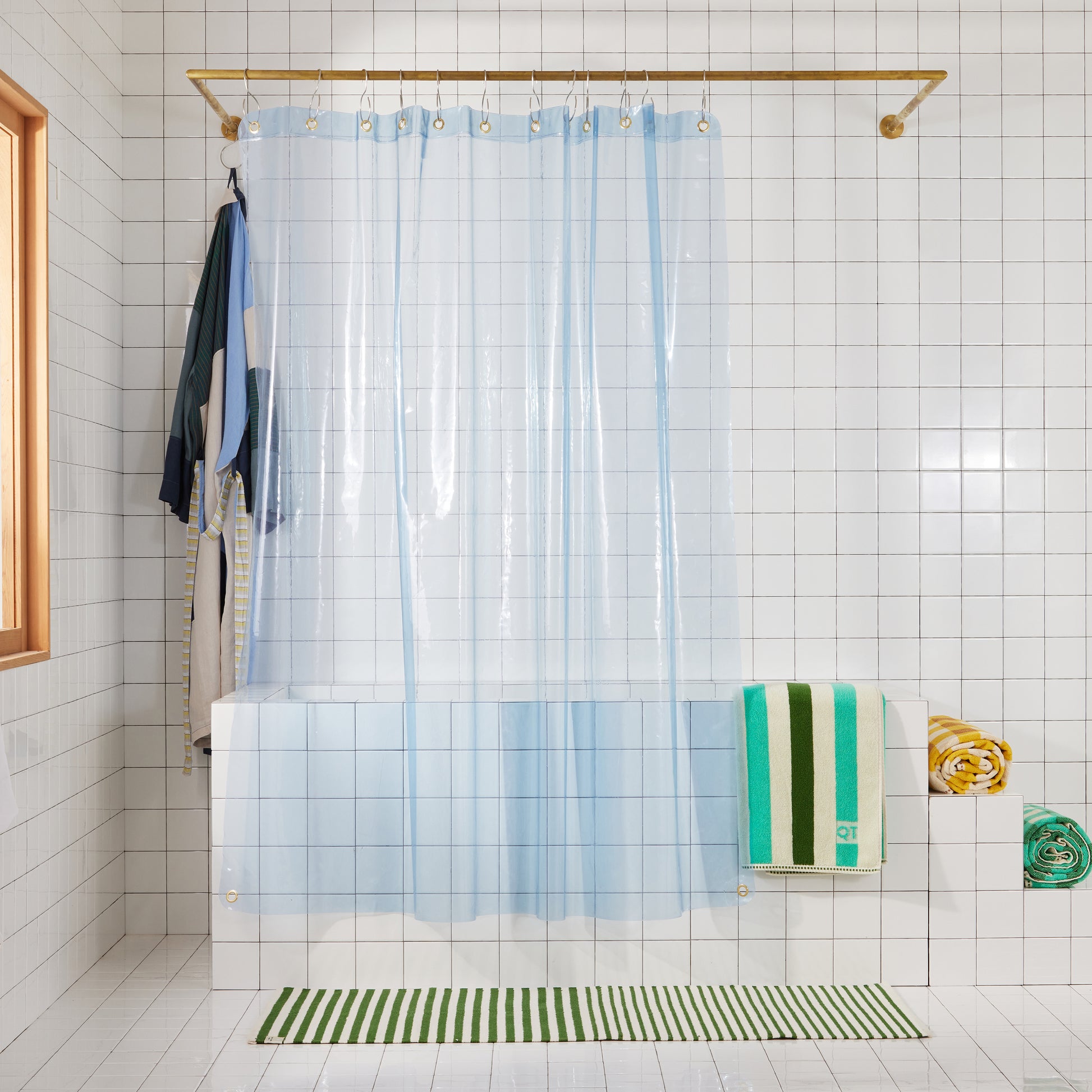 clear blue shower curtain in a Bathroom with a striped rug, and towels.