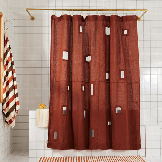Burgundy linen shower curtain with different sized rectangular window cut-outs hangs in white tiled bathroom.