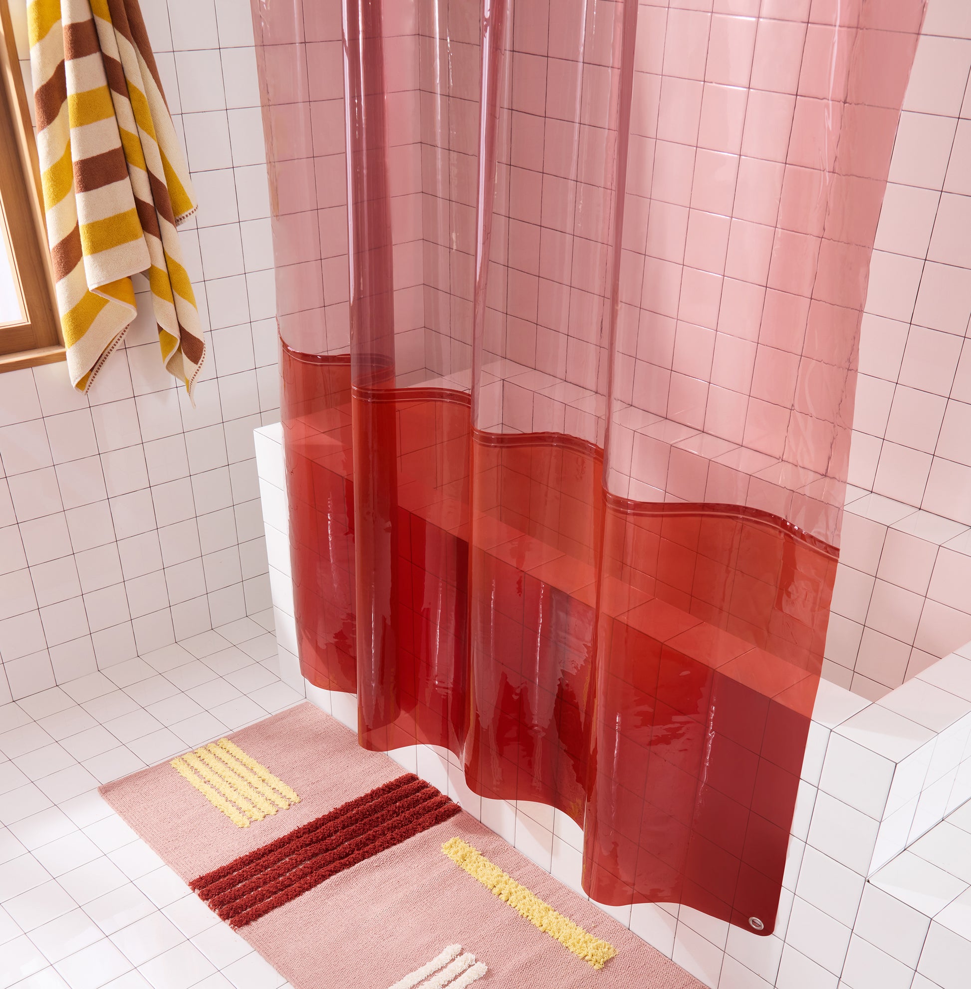 color blocked shower curtain hanging in white tiled bathroom with rose colored rug. 
