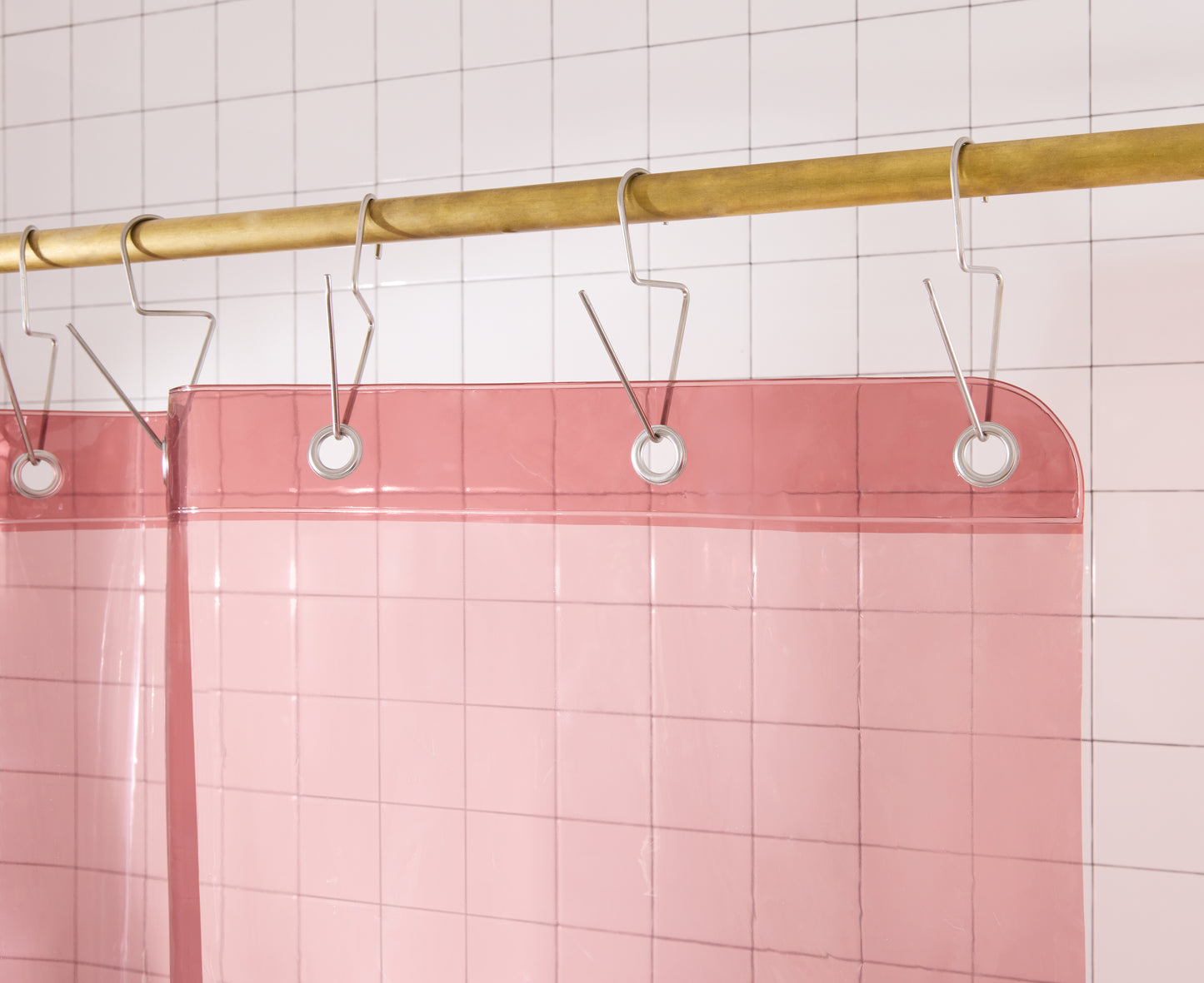 Top Hem of rose colored shower curtain hanging from brass rod. 