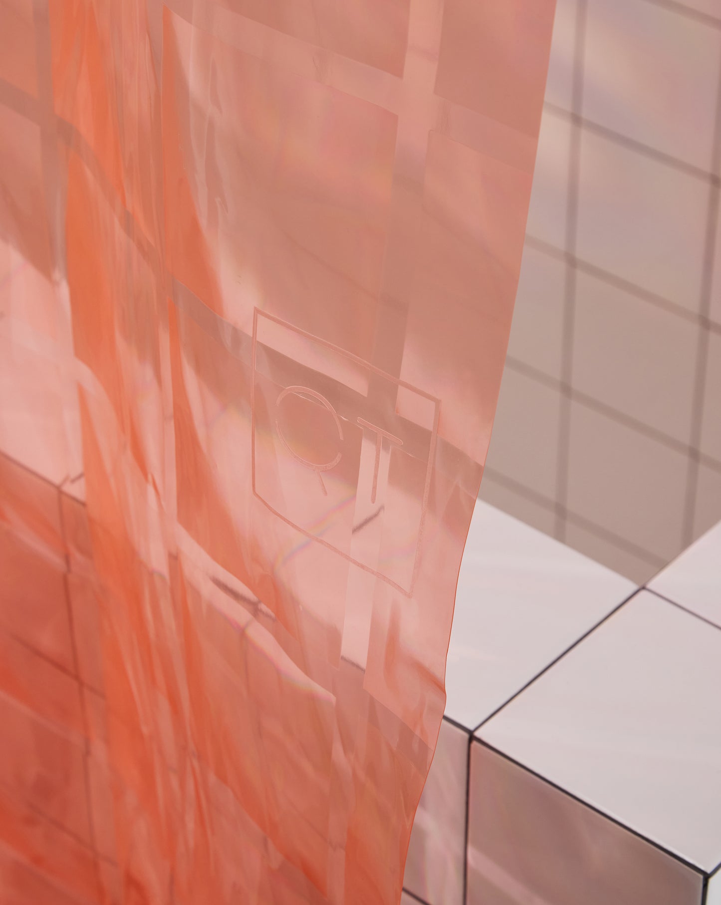 Detail of QT logo of Light pink 3D printed shower curtain hanging in white tiled bathroom.