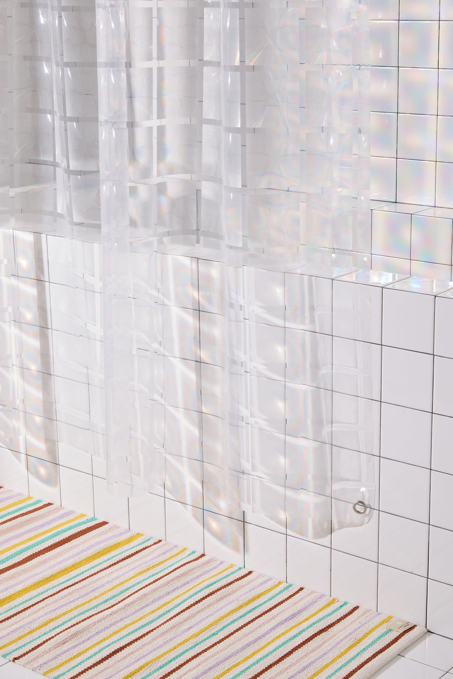 bottom corner of clear 3D curtain hanging in bathroom with white tile with colorful striped rug. 