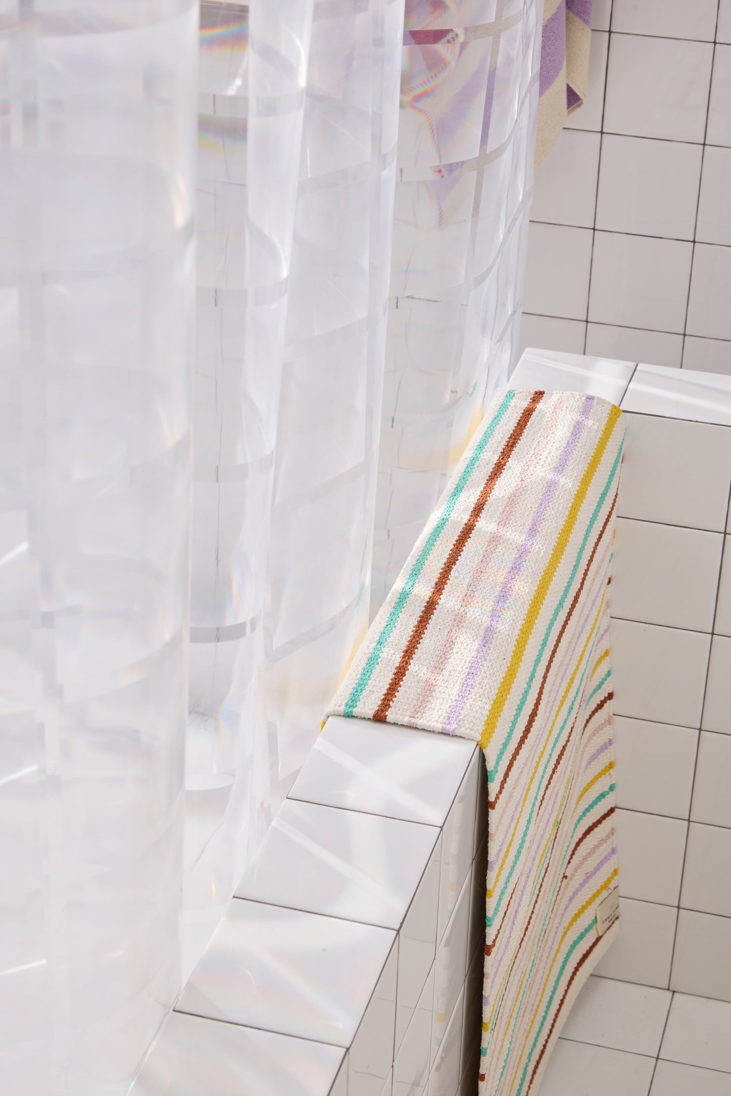 clear 3D curtain hanging in bathroom with white tile with colorful striped rug. 