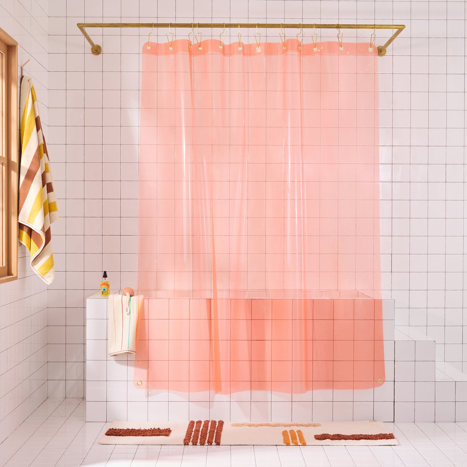 Sun shower curtain in peony hanging over bathtub styled in a white tiled bathroom with rose reyes rug and catalina bath sheet in canyon.