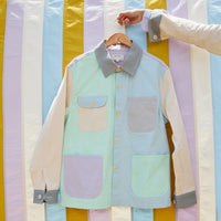 Pastel-colored color-blocked jacket with pockets on a hanger against a striped background