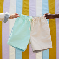 a pairs of shorts, one side limint green and one other beige, held up against a colorful striped background.