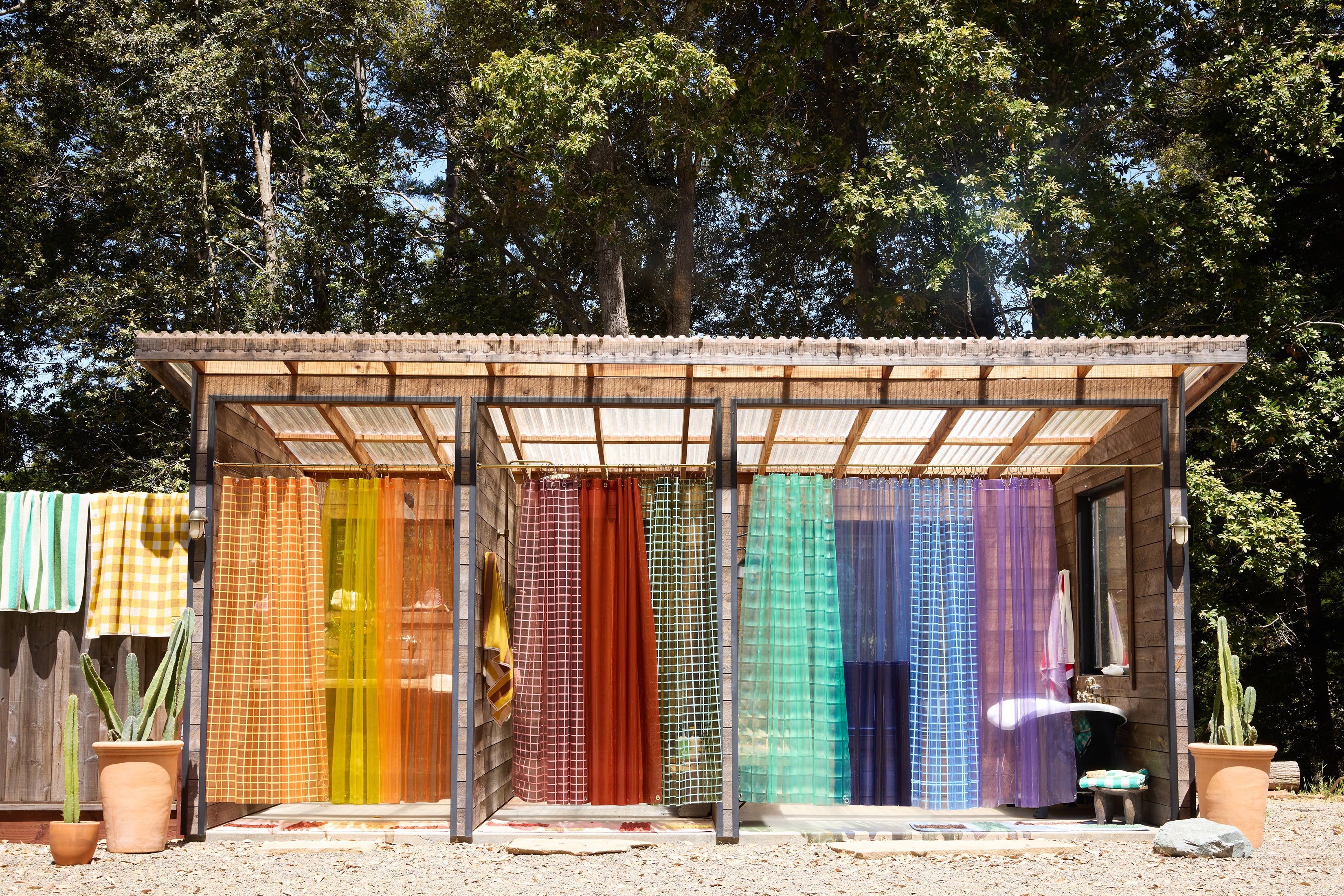 Colorful curtains hanging outdoors with a wooden structure and trees in the background